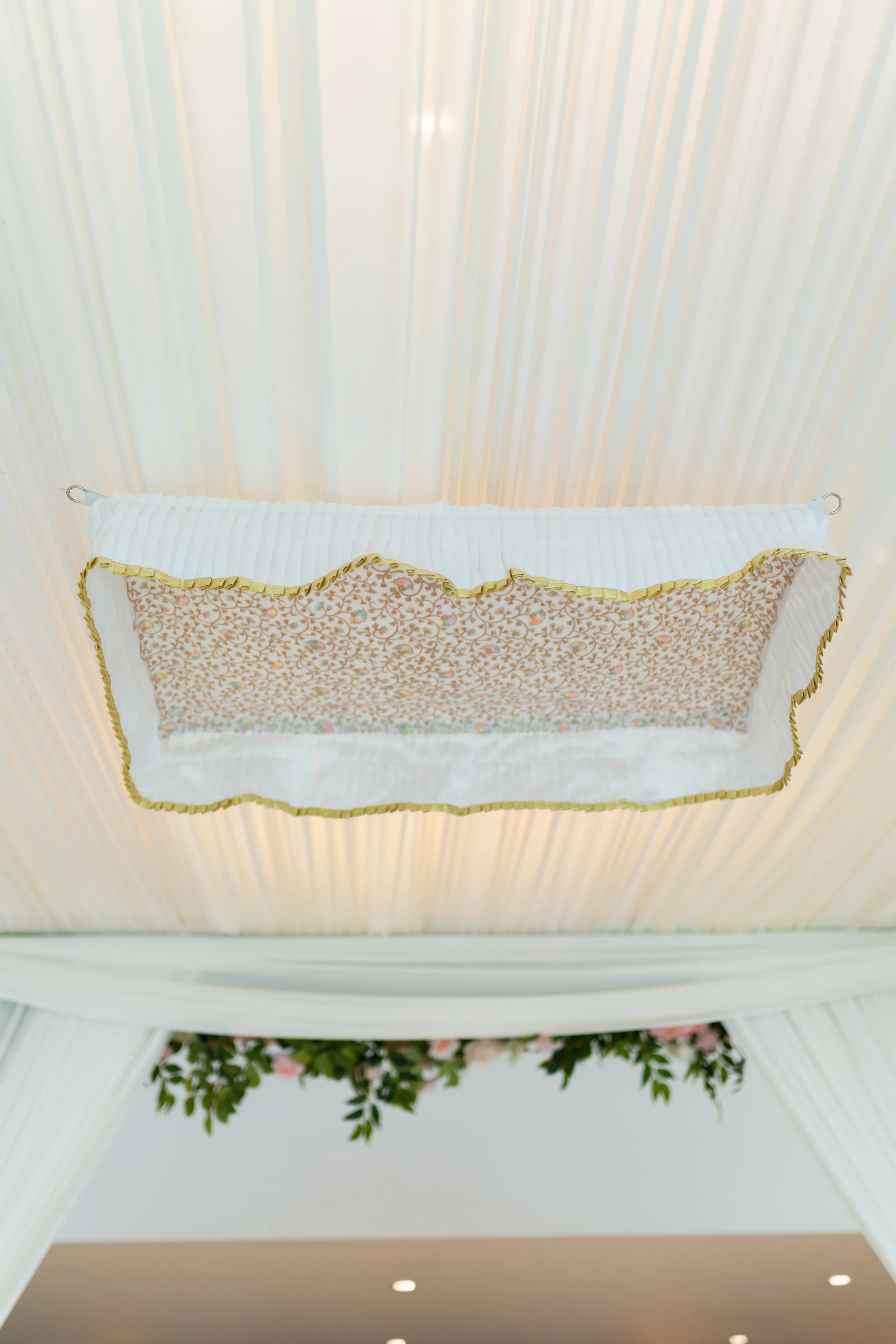 Ceiling-mounted light fixture with a decorative fabric shade hanging from a ceiling with vertical pleated drapes and floral decorations.