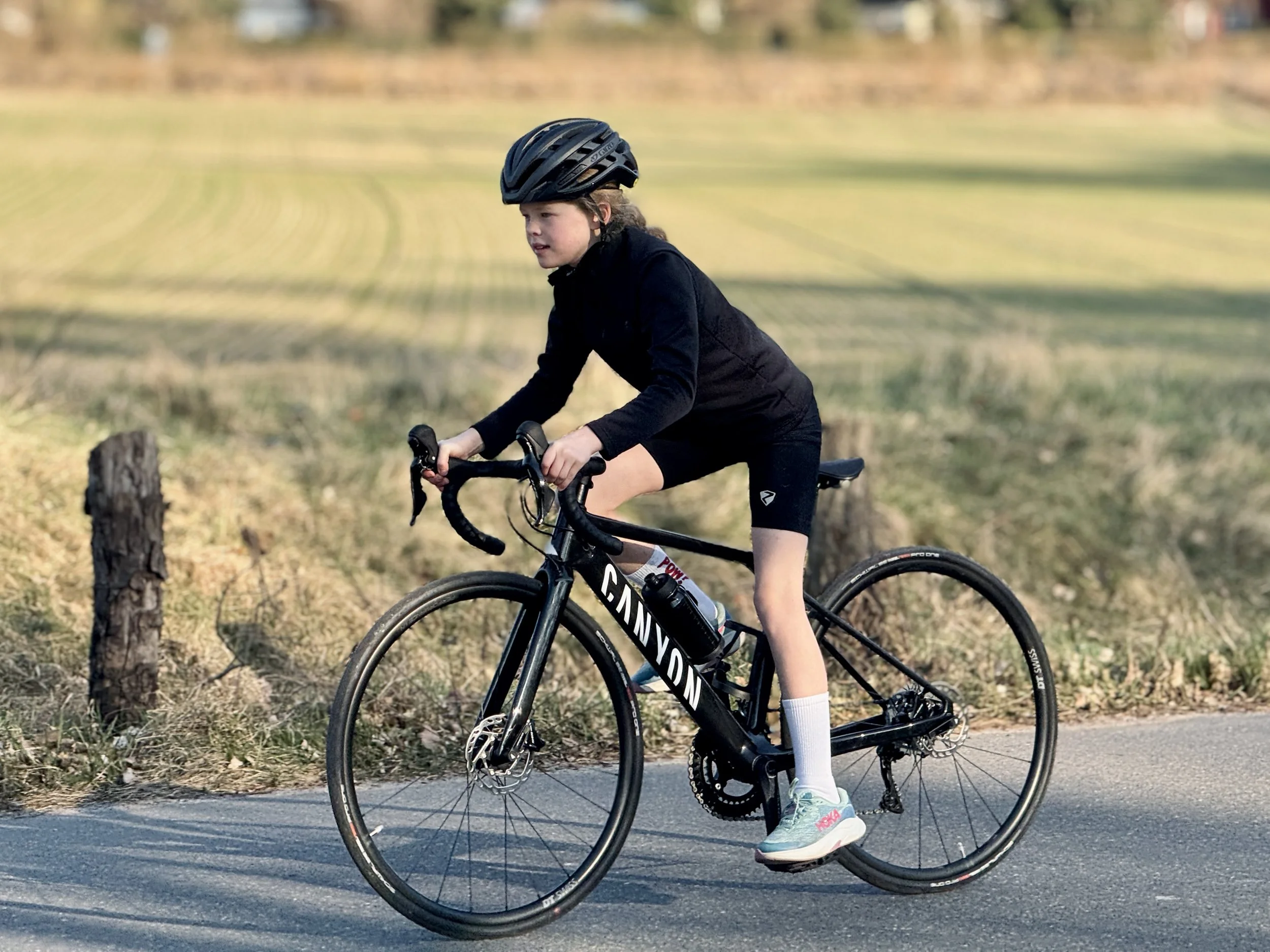 Mädchen auf schwarzen Canyon Rennrad im stehenden Fahren mit Feldern im Hintergrund