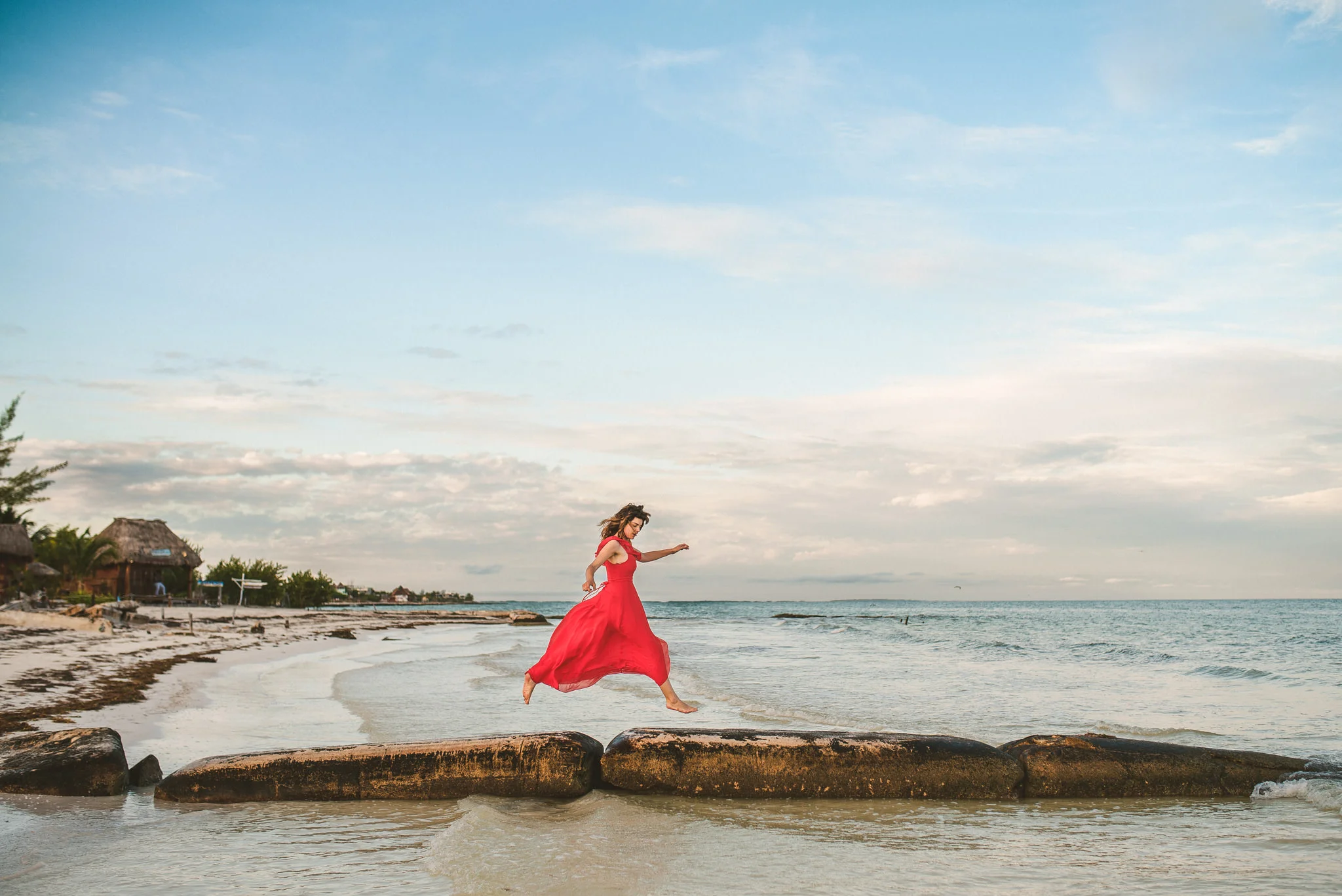 mujer con vestido rojo saltando por la playita