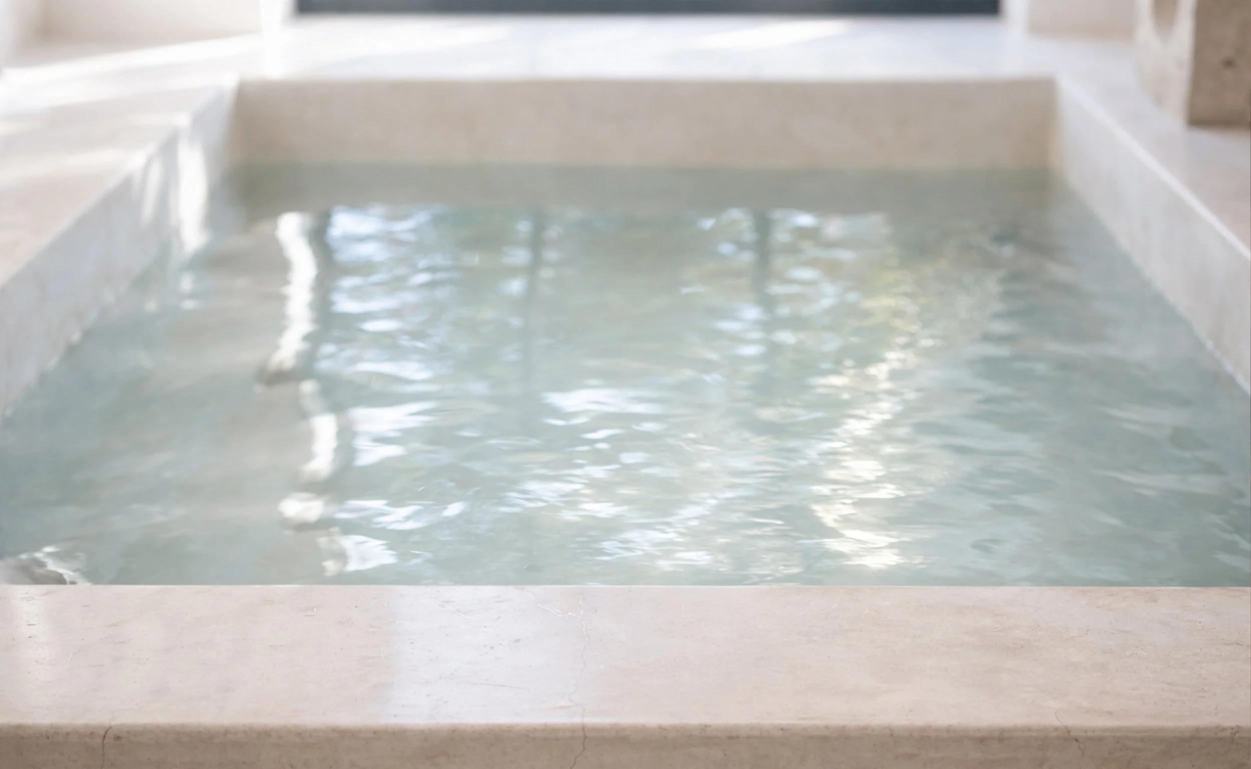 Still bath water illuminated by soft natural light, representing continuity and restraint within ritual-led care