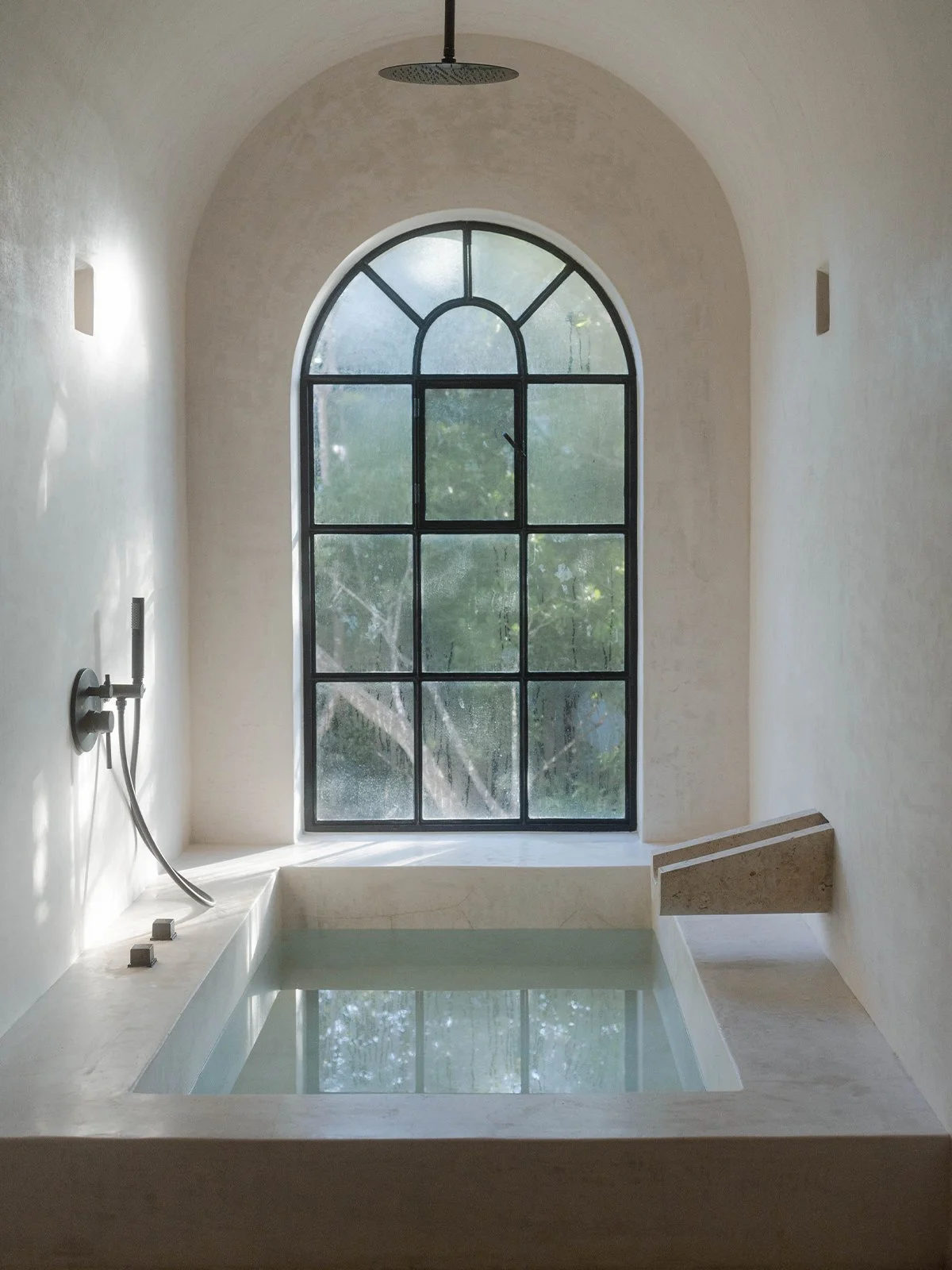 Serene architectural bath filled with still water beneath an arched window, symbolising the quiet presence and reflective calm of V&M SPA rituals.