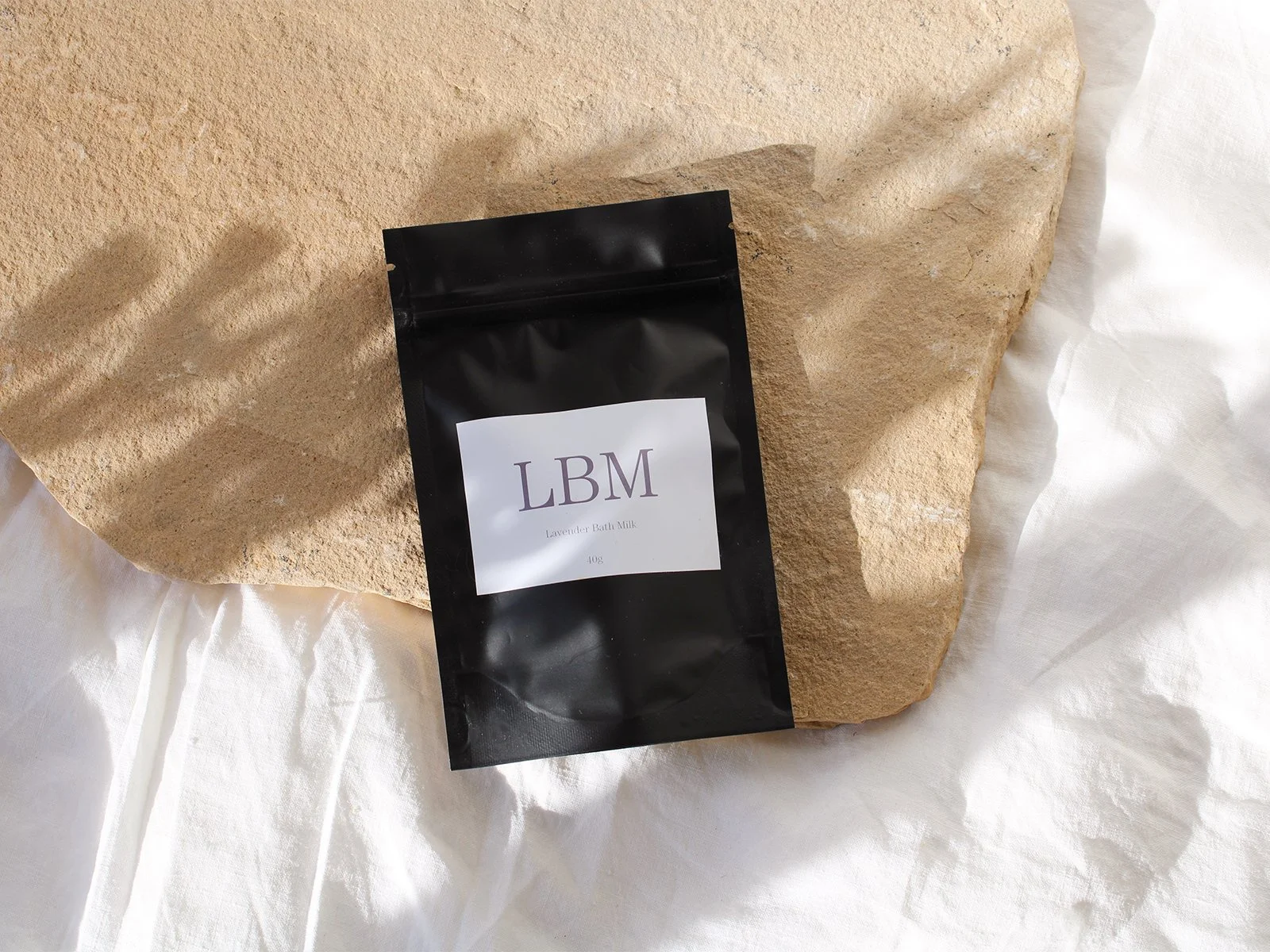 Bath Milk sachet and candle styled on linen, symbolising calm restoration before the holiday season.