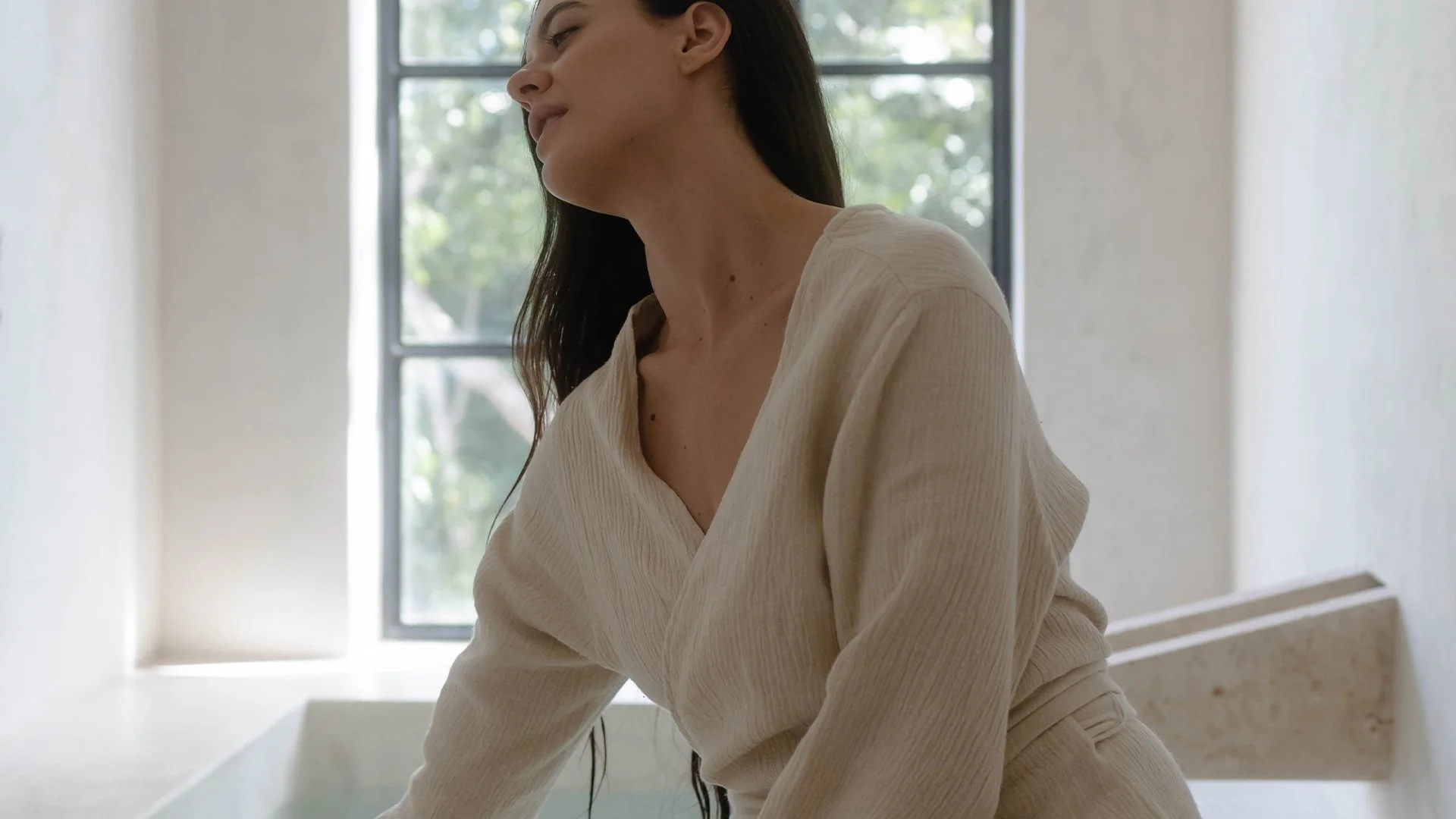 Arched window illuminating a stone bath with soft natural light in a calm, minimalist spa setting