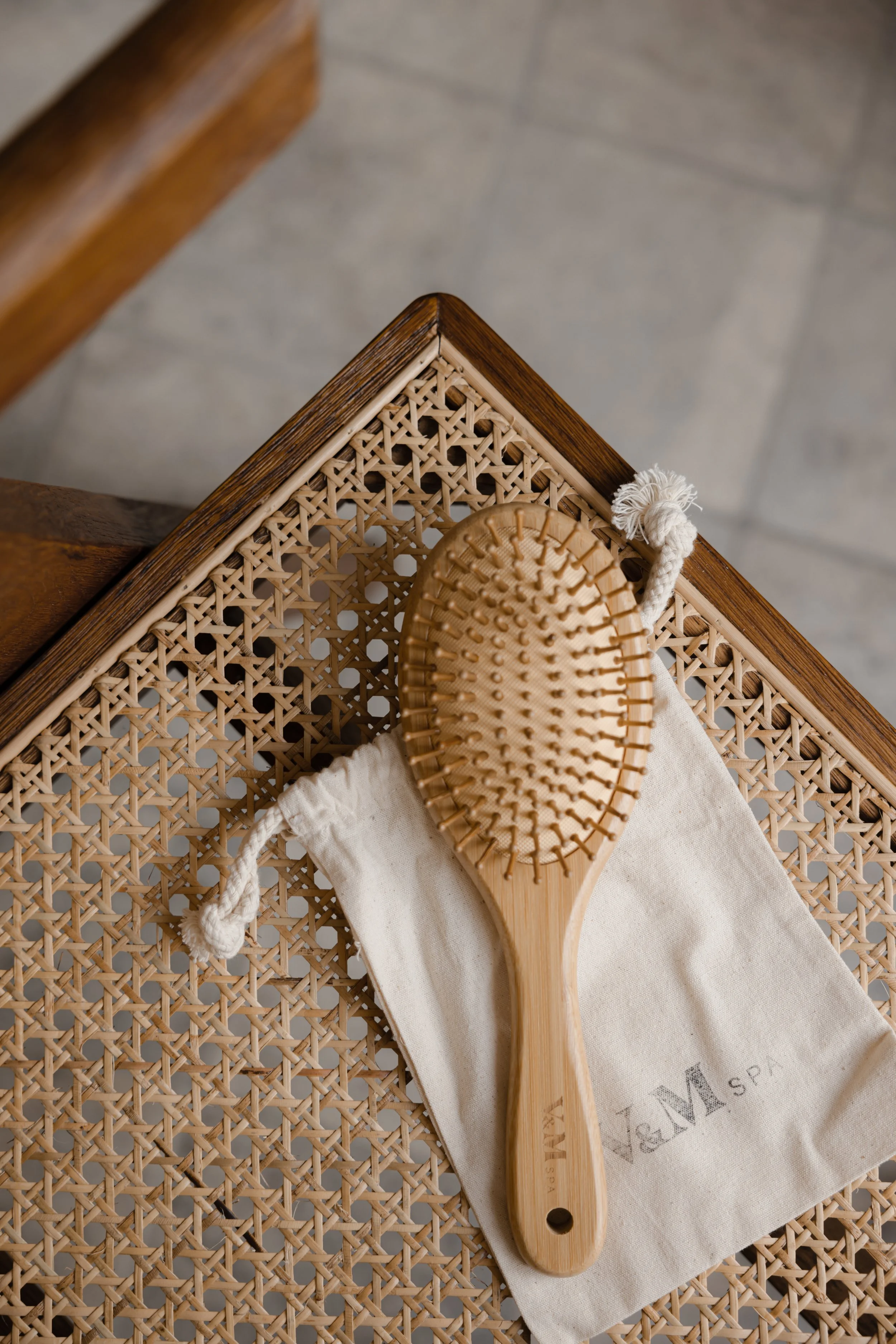 Wooden hairbrush resting on a folded cloth pouch on a woven chair, lit by soft natural light.