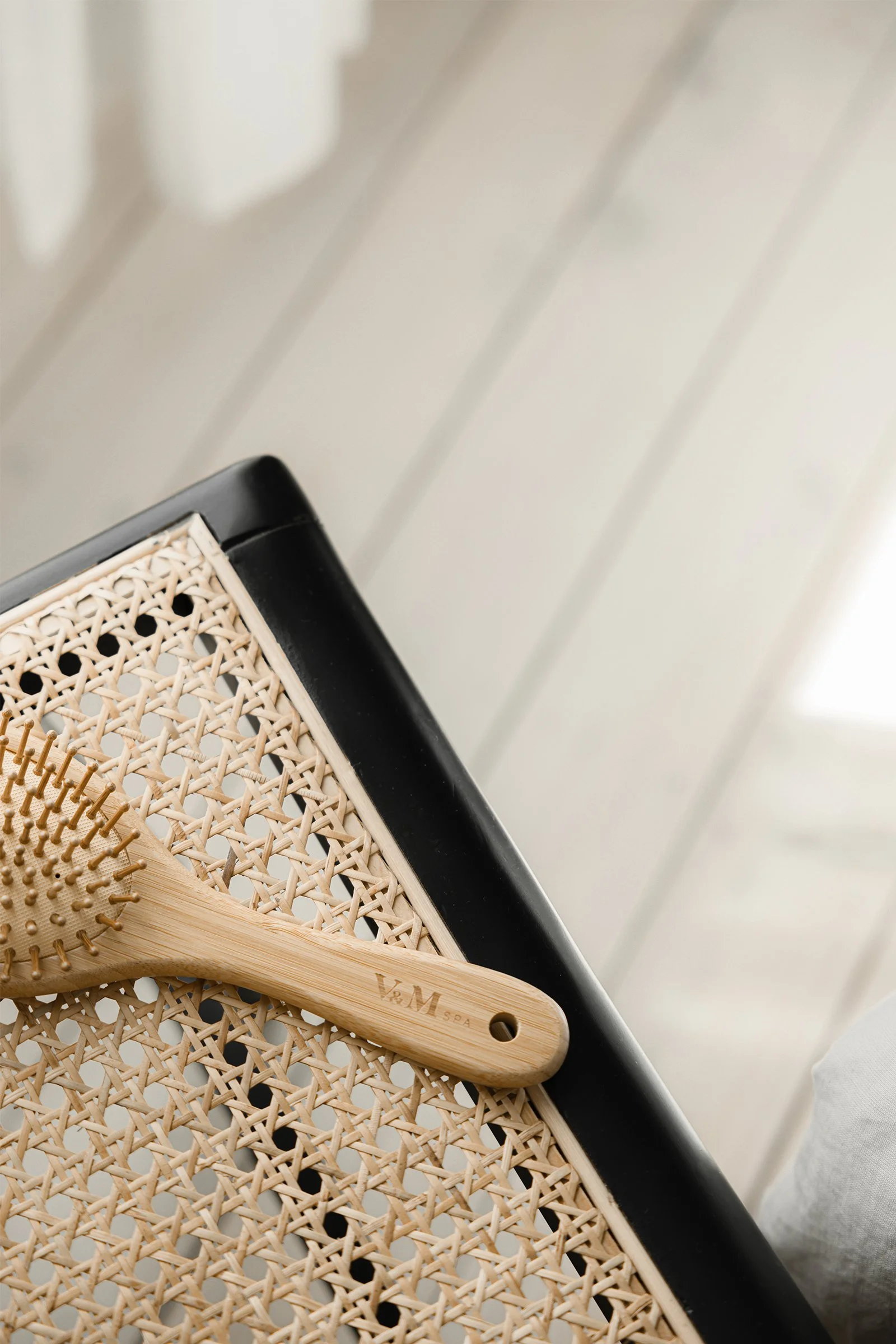 Wooden hairbrush resting on a woven chair in natural light, symbolising restraint and stillness in hair care