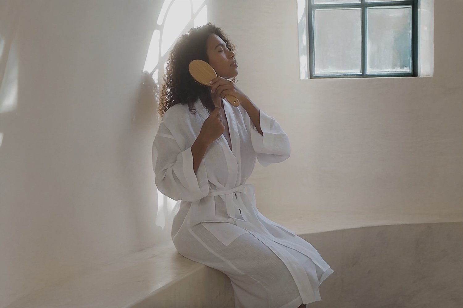 Person in robe brushing hair with V&M SPA Wooden Hairbrush after a winter bathing ritual — complete restoration routine