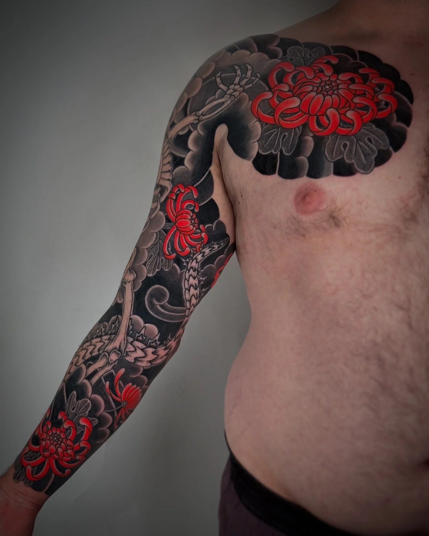 A person's upper body with a colorful tattoo sleeve featuring red and black flowers, a dragon, and a serpent on their shoulder, arm, and chest.