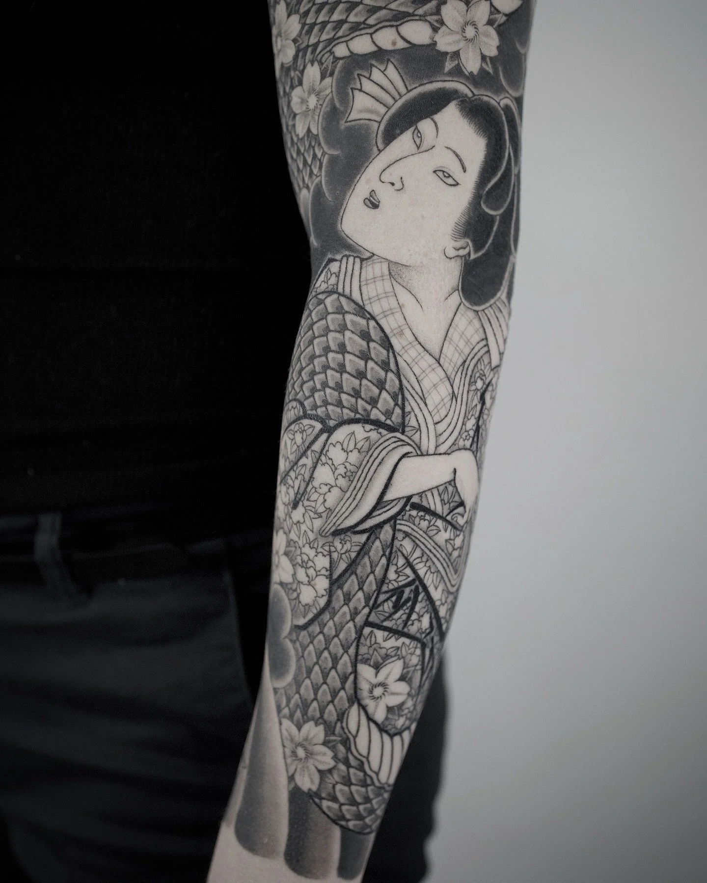 Black and white tattoo of a woman in traditional Japanese clothing with a parasol, with floral and wave patterns.