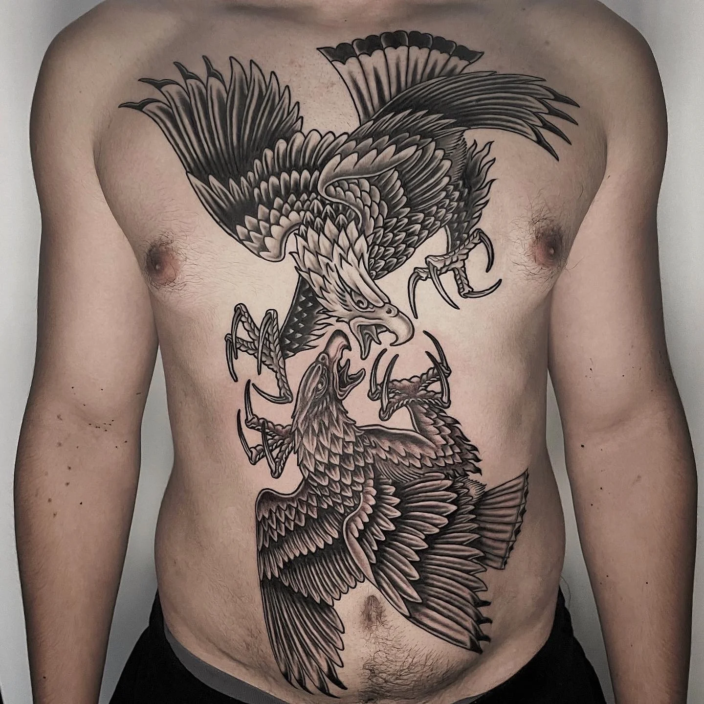 Black and grey tattoo of two fierce eagles with sharp beaks and claws on a person's chest.