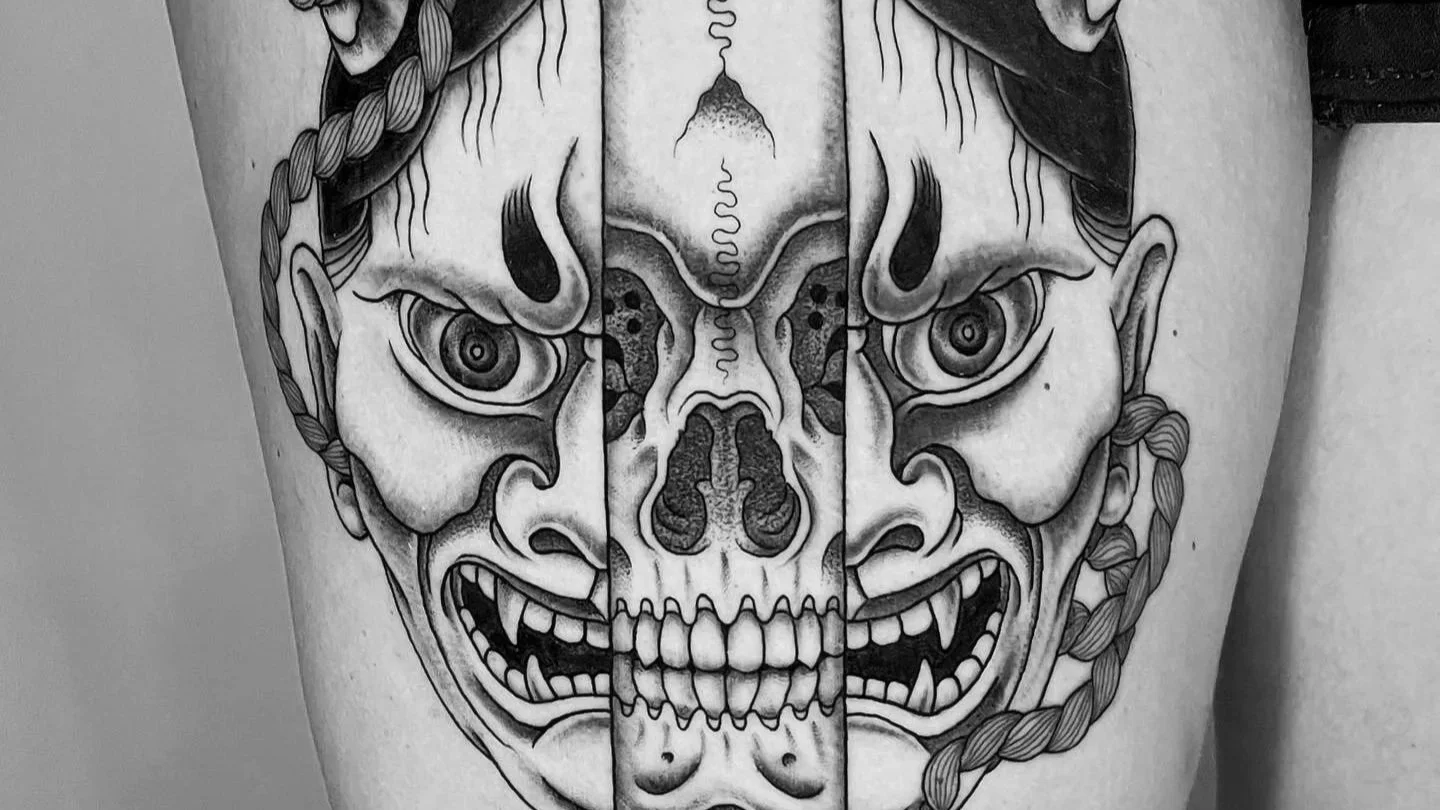 Black and gray tattoo featuring a split design with a human face on each side, one representing a demonic or monstrous face with sharp teeth and the other a skeletal face with hollow eyes, connected by a central skull imagery.