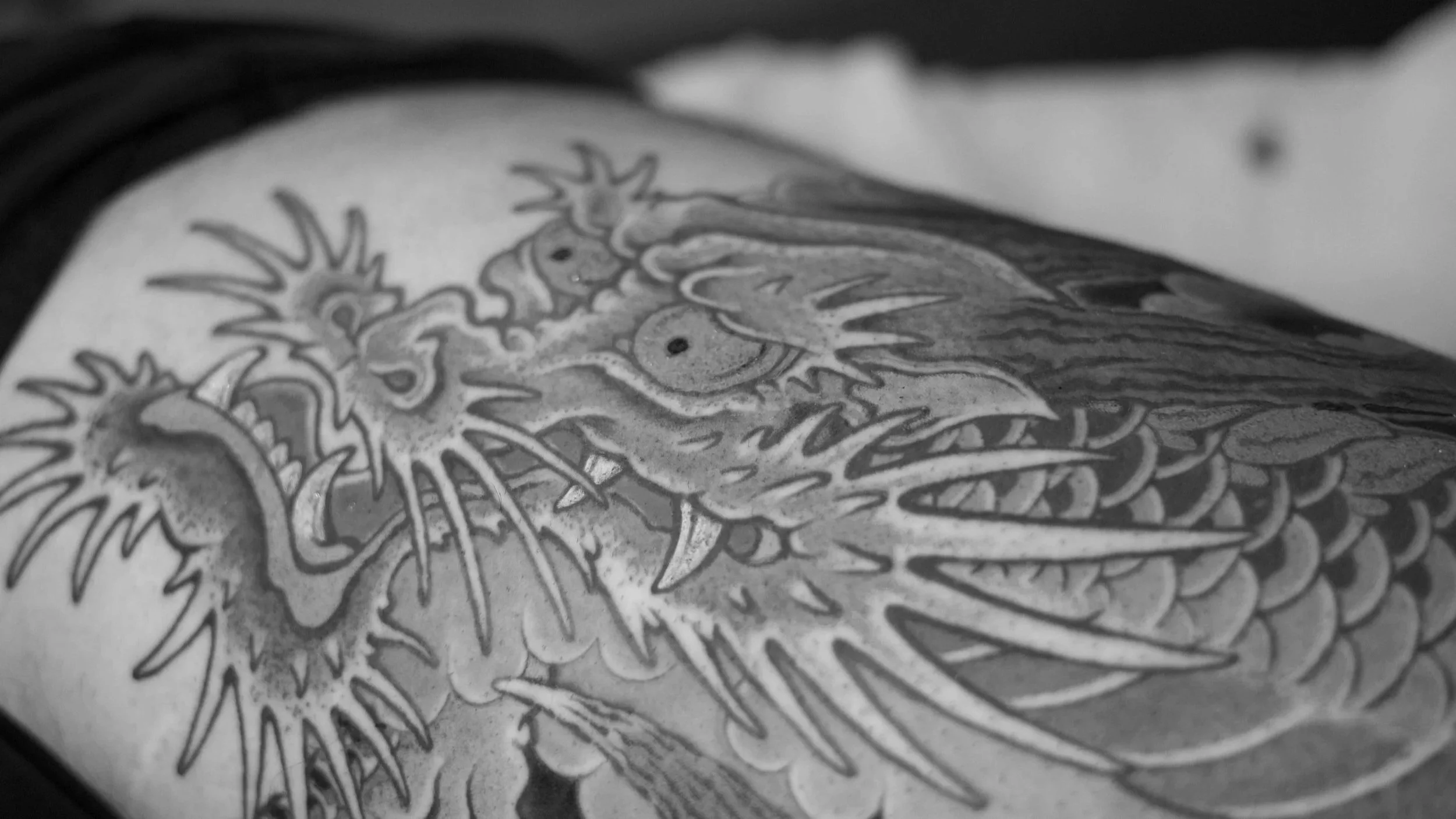 A detailed black and white tattoo of a dragon with intricate scales and flames, occupying most of the person's arm.