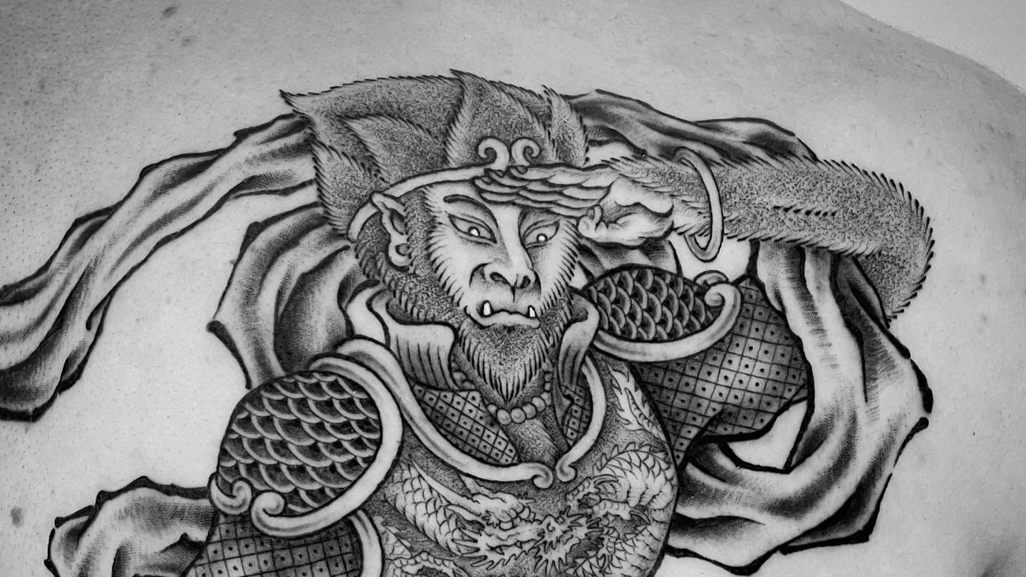 Black and gray tattoo of a fierce warrior with a beastly face, wearing armor, saluting with one hand and a cape flowing behind.