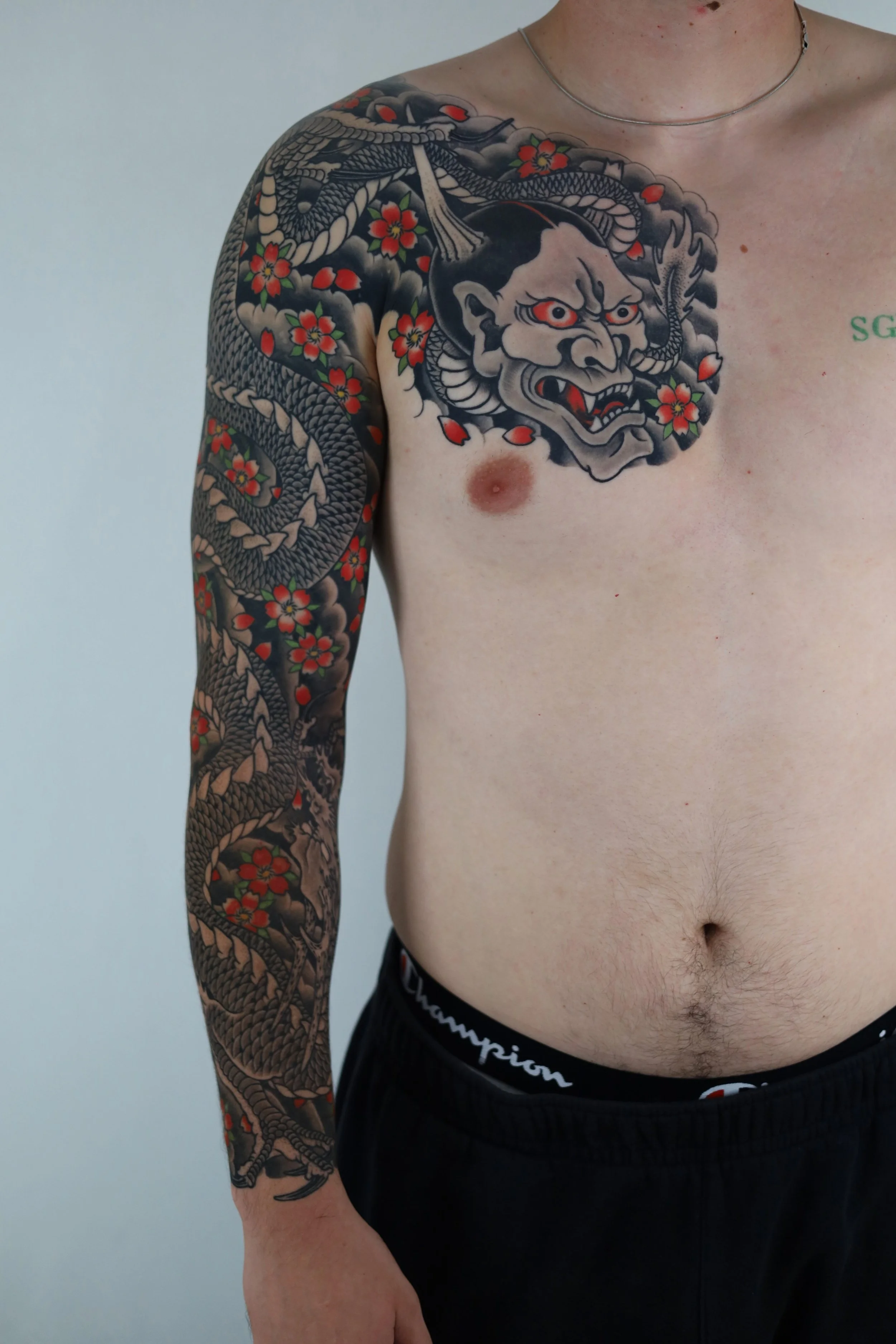 Person with a large Japanese-style dragon and demon face tattoos on the upper chest and arm.