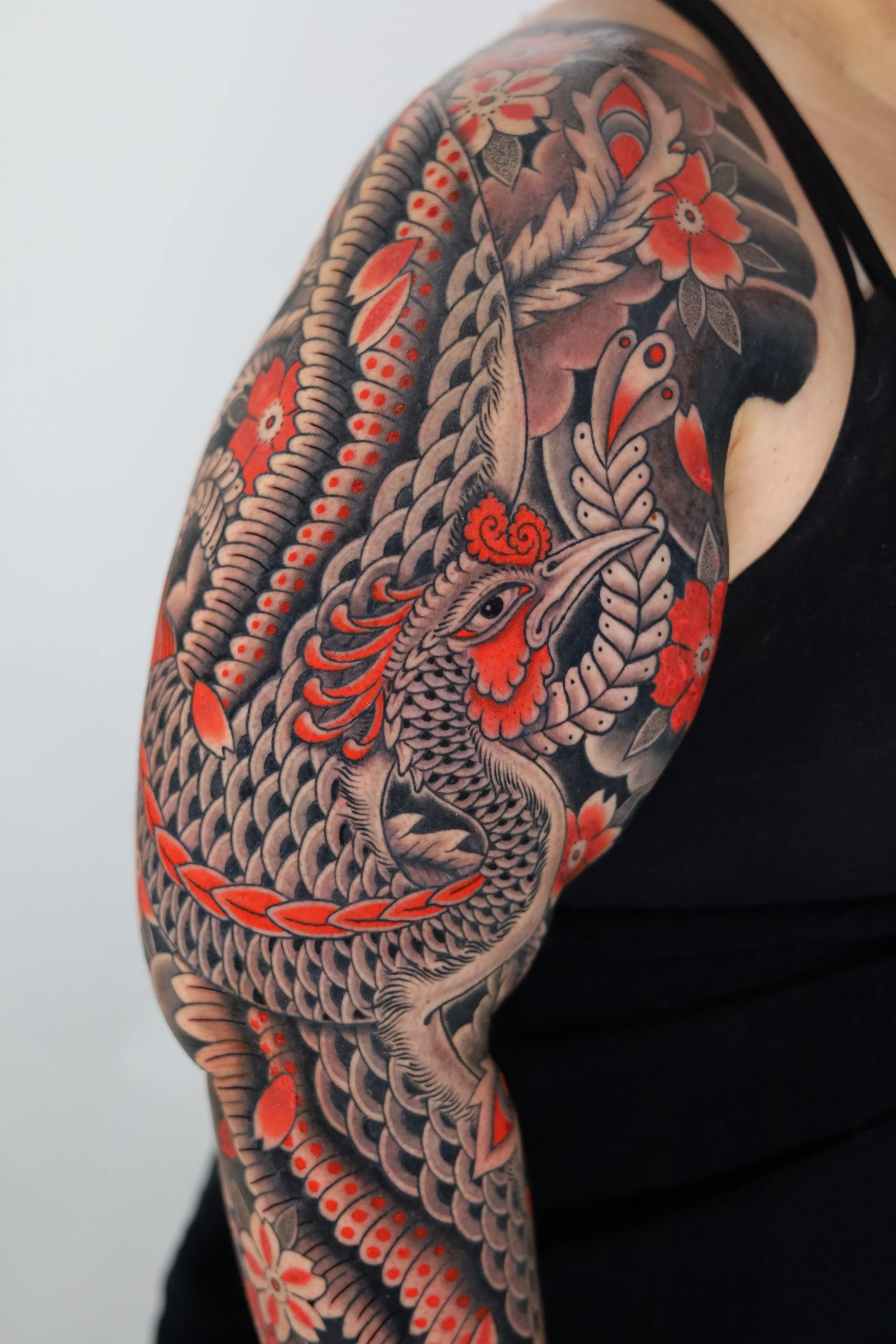 Colorful Japanese-style sleeve tattoo of a snake intertwined with flowers, featuring black, gray, red, and orange ink.