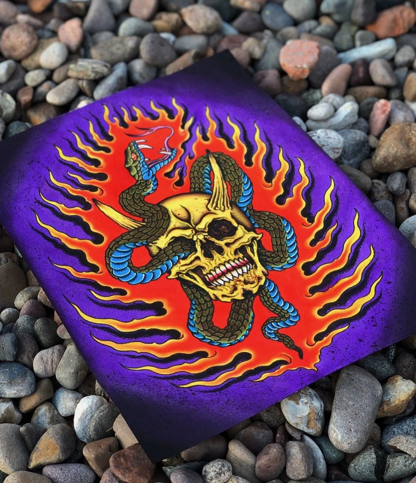 A vibrant tattoo-style artwork of a skull with a snake coiled around it, surrounded by flames on a purple background.