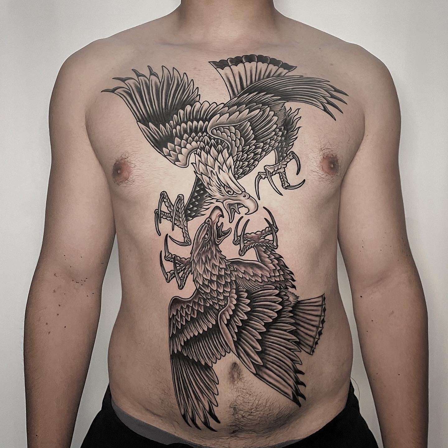 A man's chest featuring a large, detailed tattoo of two eagles with their wings spread, claws out, and beaks open.