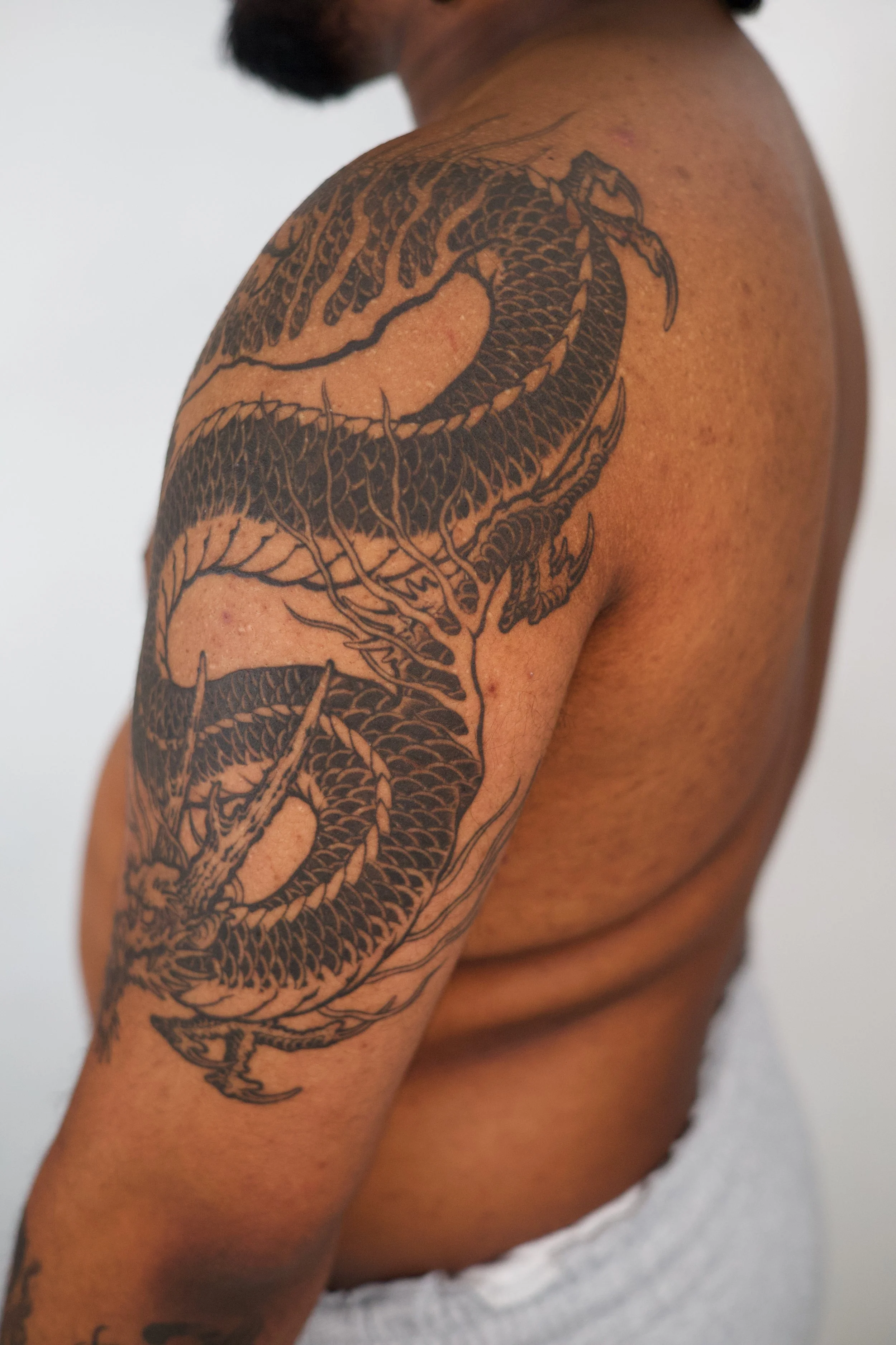Close-up of a person's upper arm and shoulder with a detailed black tattoo of a dragon.