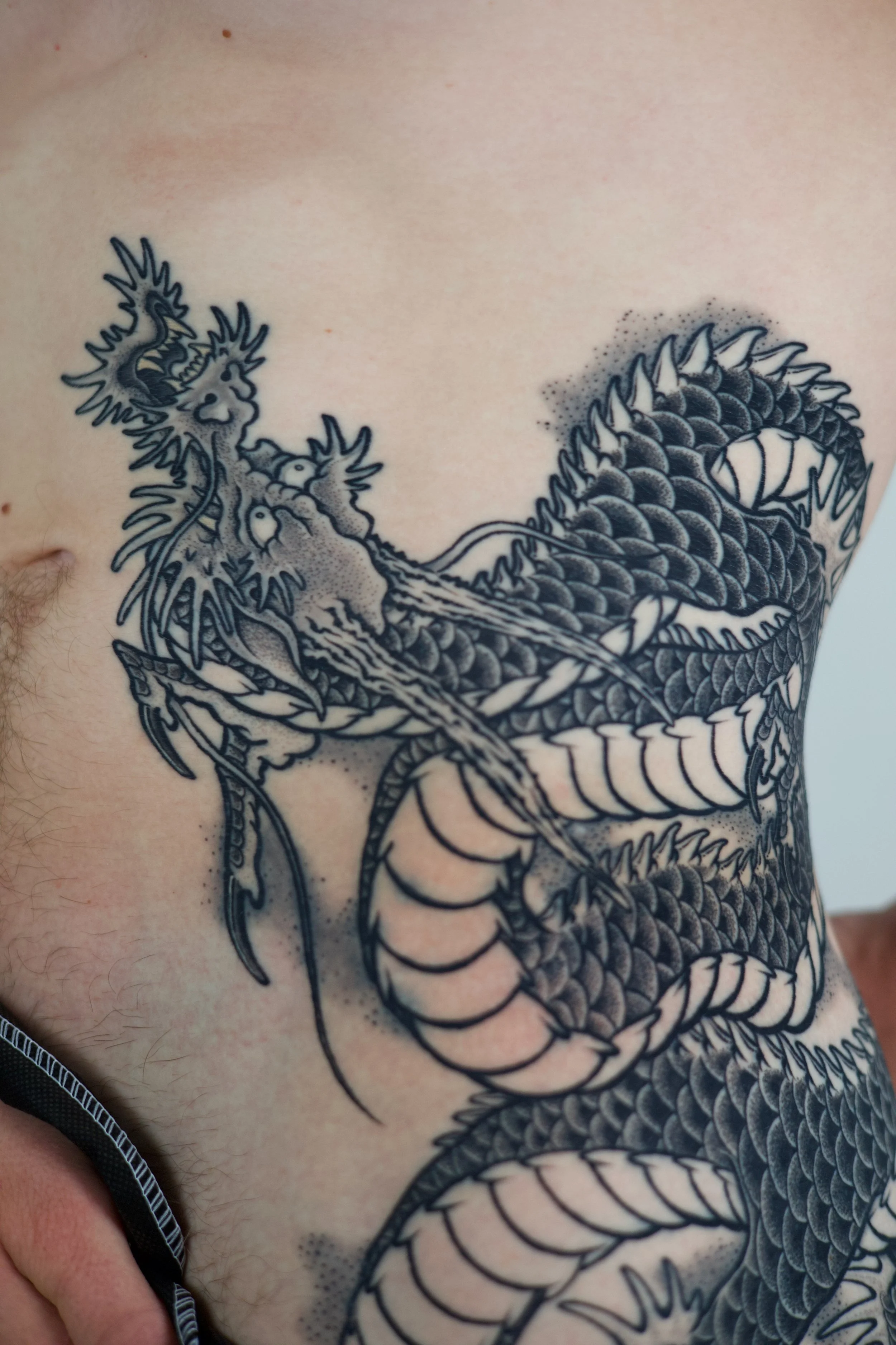 Black and grey detailed dragon tattoo on person's chest and side.