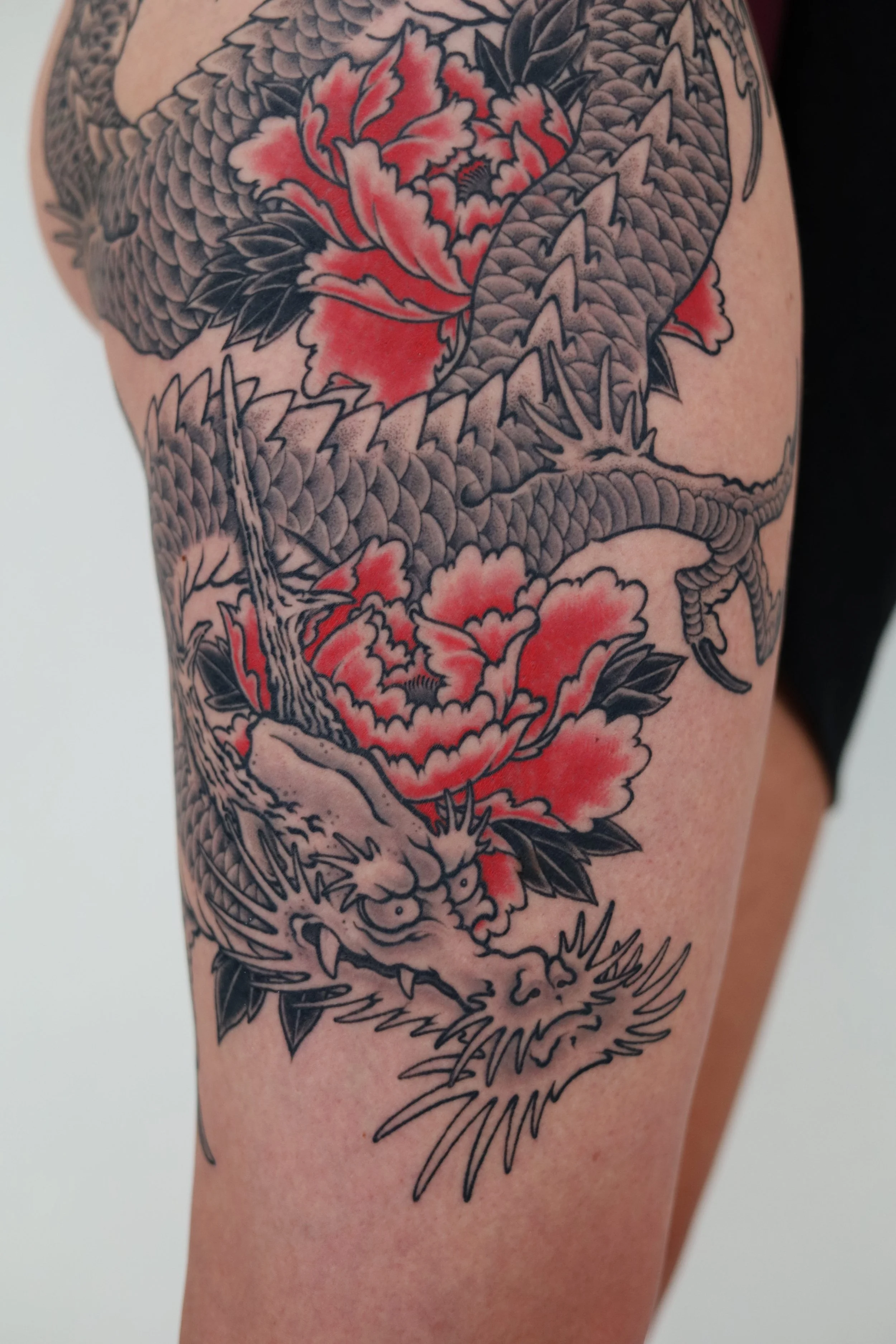 Tattoo of a dragon intertwined with red and pink flowers, with detailed scales and fierce facial expression.
