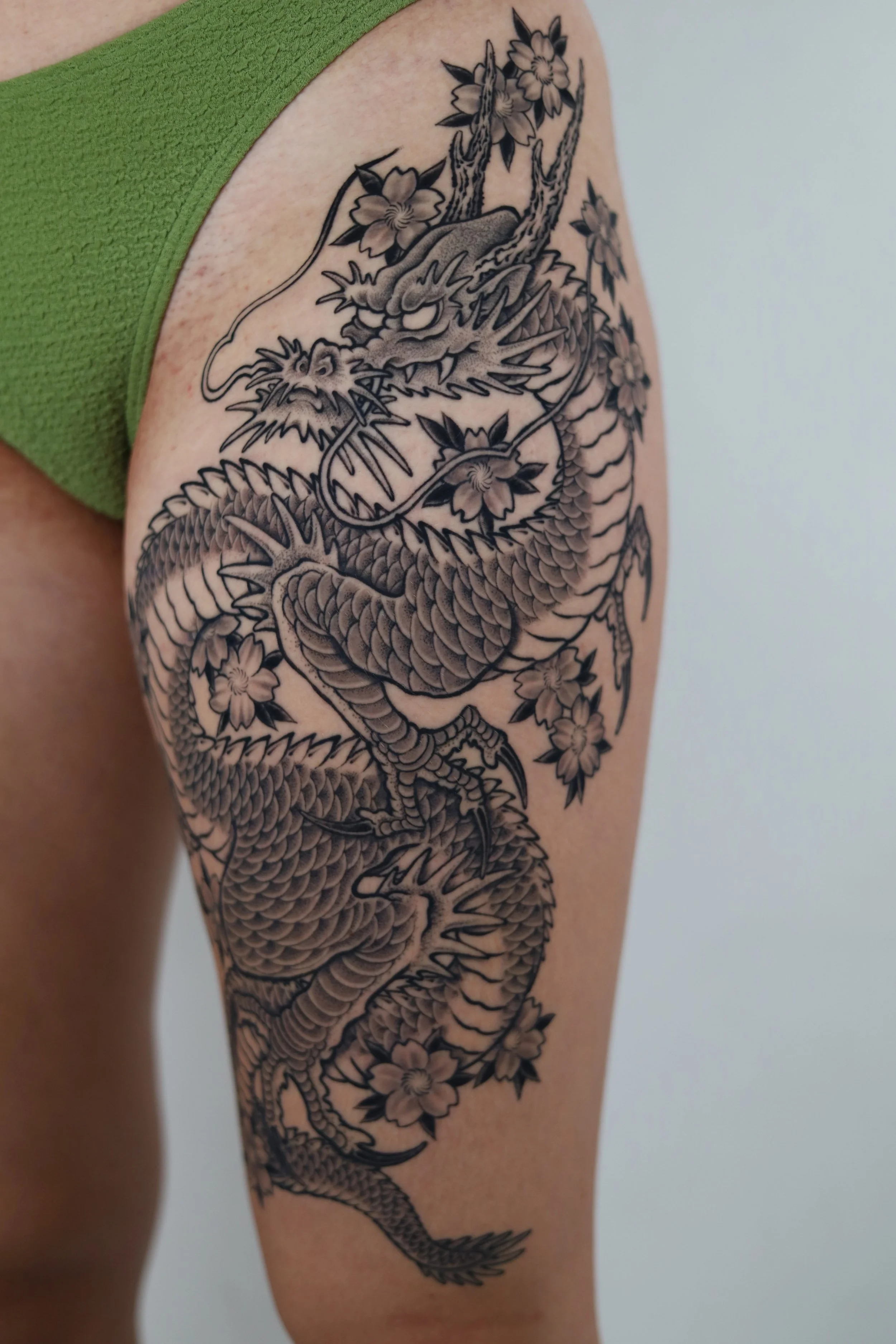 Black and gray tattoo of a dragon with floral accents on a person's upper arm and shoulder.