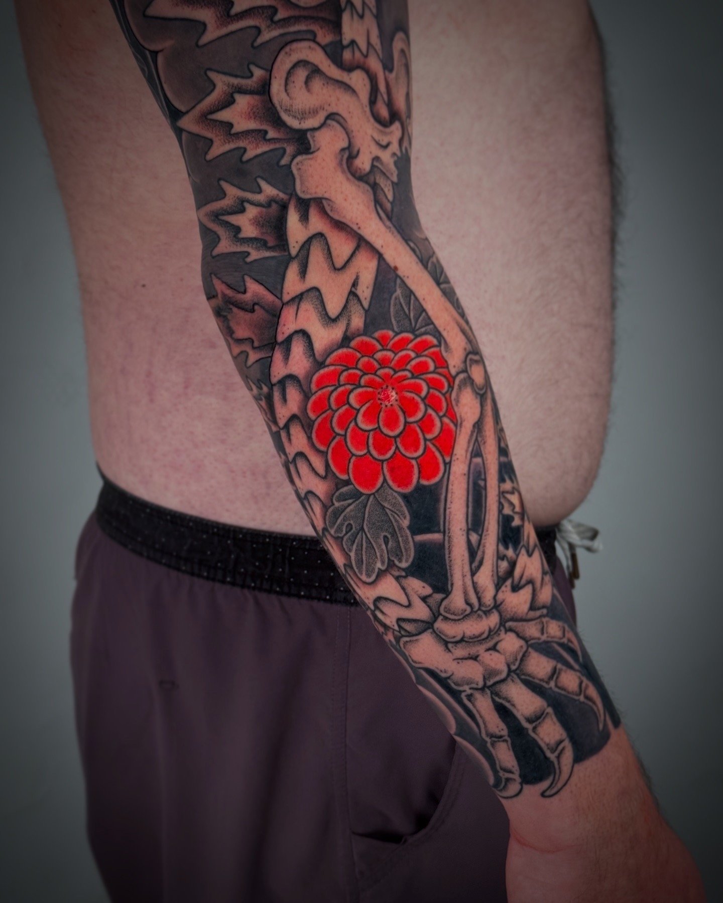 Tattoo of a bird skull with a red flower and dark leaves on a person's arm.