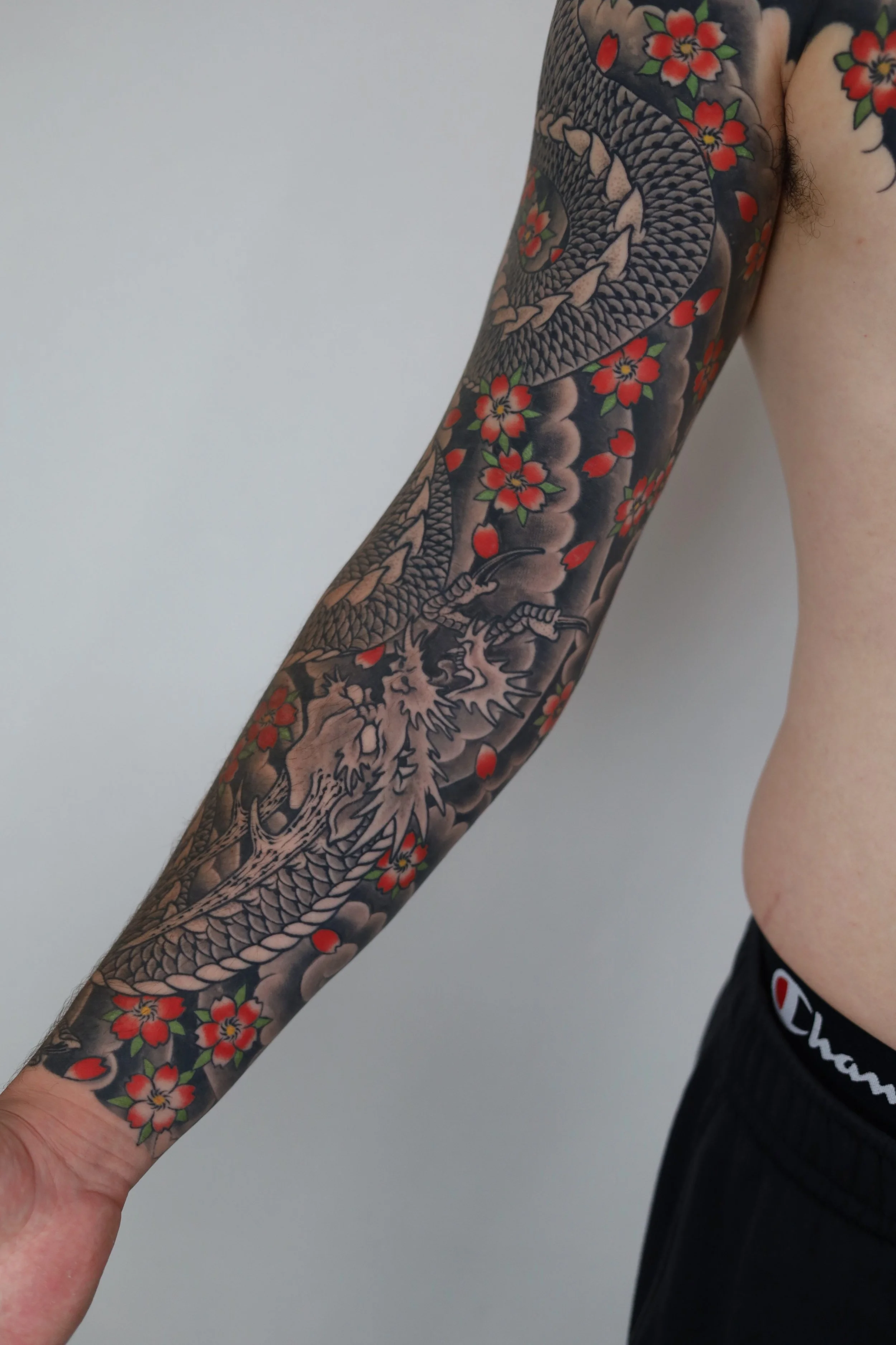 Angelina dragon tattoo on man's arm with red and pink flowers
