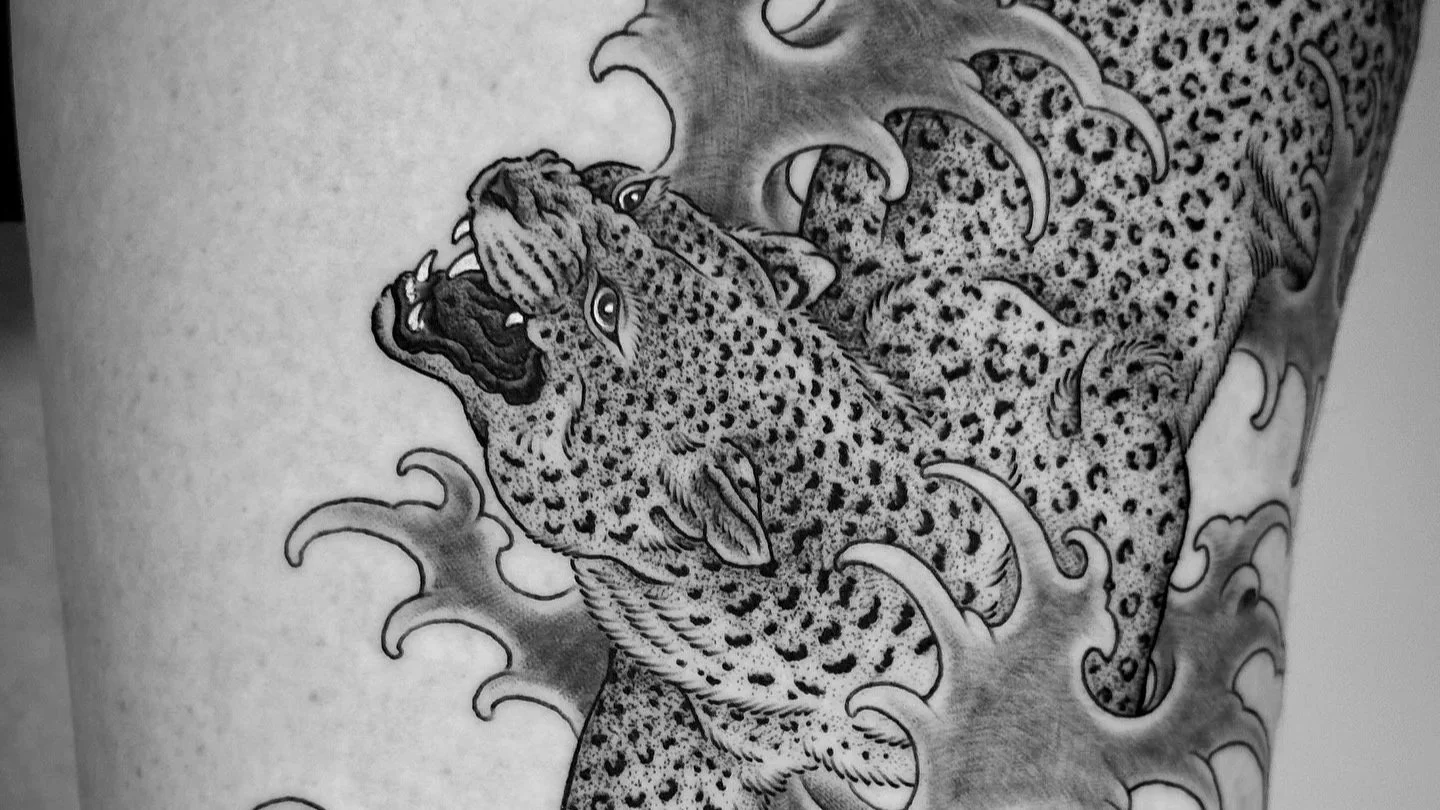 Black and gray tattoo of two fierce, detailed jaguars with open mouths and sharp teeth, surrounded by swirling water or smoke patterns.