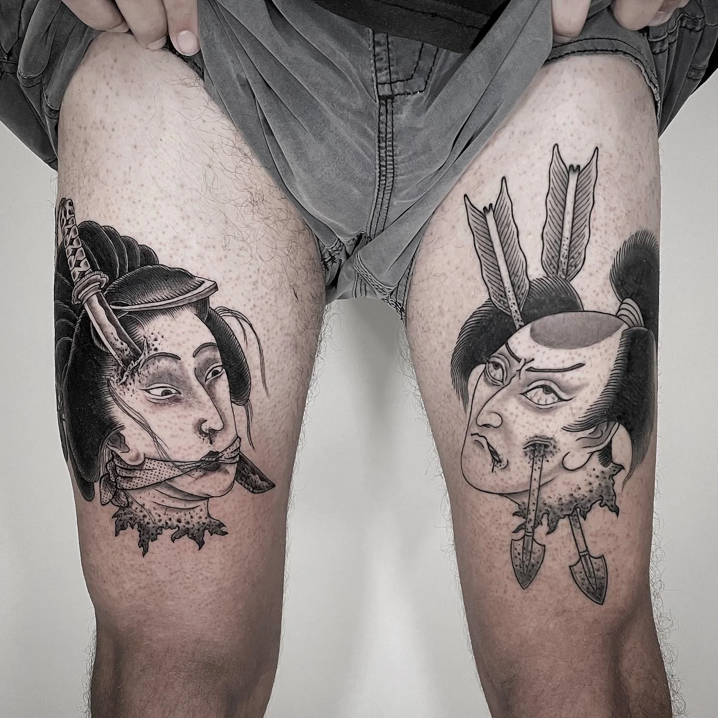 Tattoo of two traditional Japanese masks on the person's thighs, featuring detailed line work and shading.