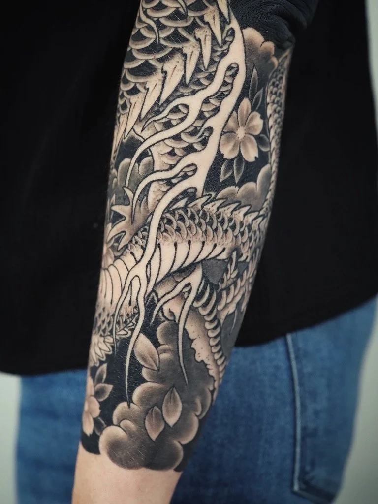 Black and white sleeve tattoo featuring a dragon, flowers, and clouds.