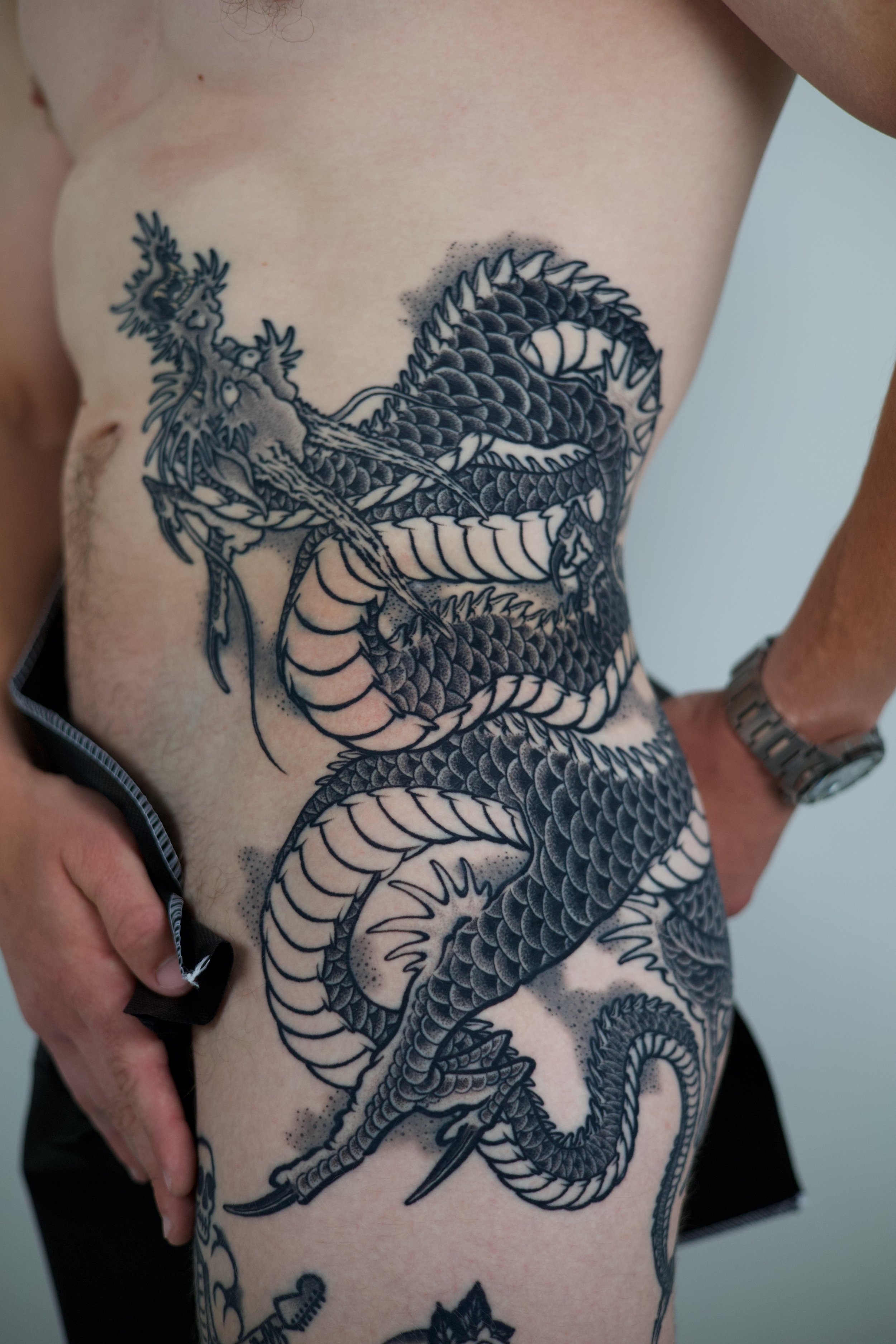 Black and gray tattoo of a dragon on a person's side and torso.