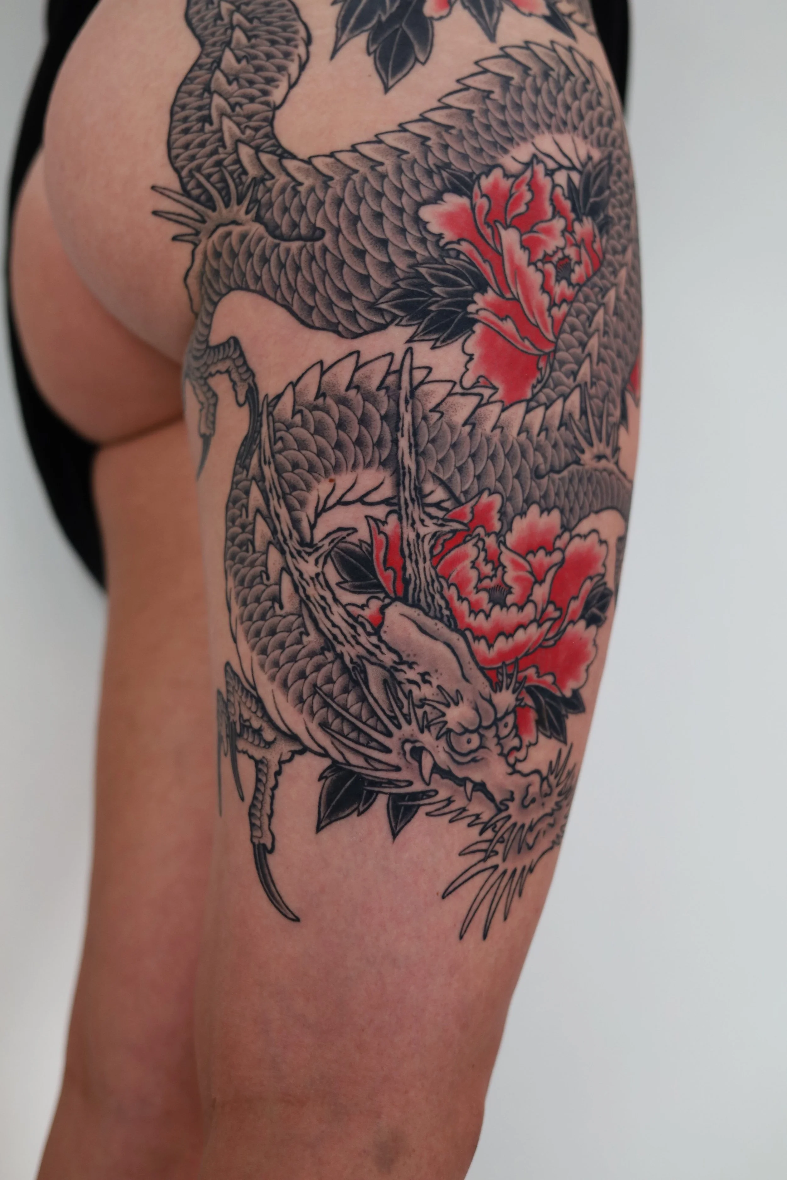 Tattoo of a dragon intertwined with blooming flowers on a person's upper arm and shoulder.