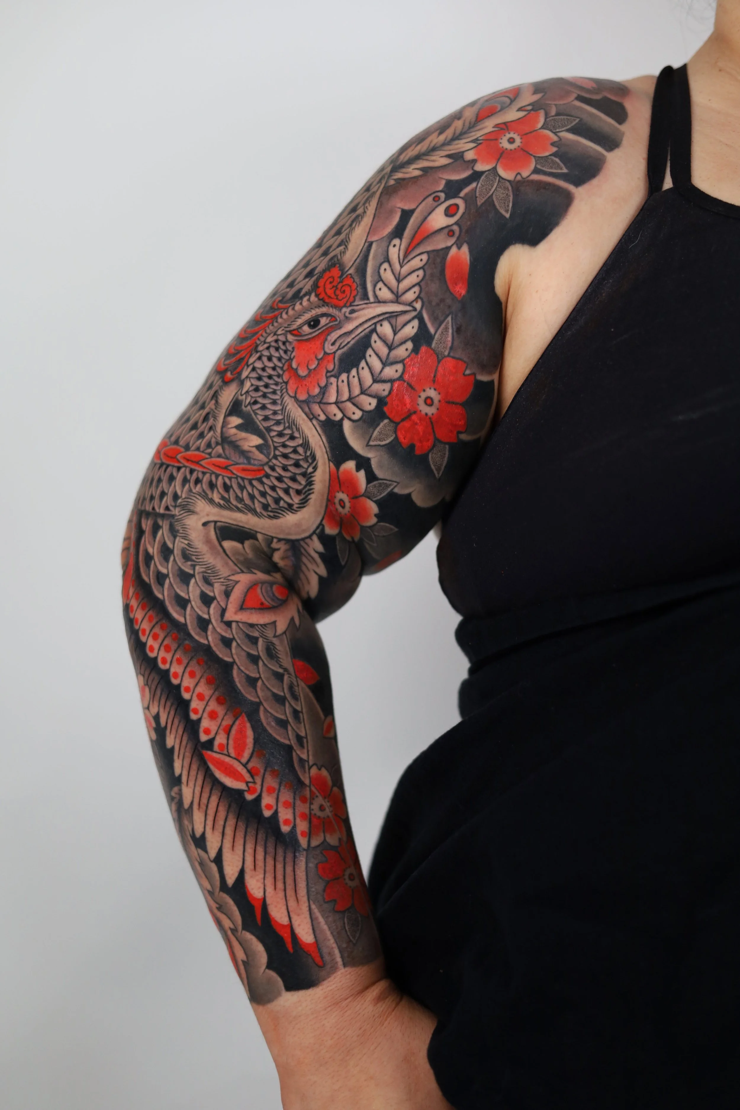 Tattoo sleeve featuring a stylized bird with red flowers and detailed black shading.