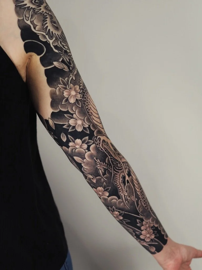 Tattoo sleeve featuring cherry blossoms and a dragon on a person's arm.