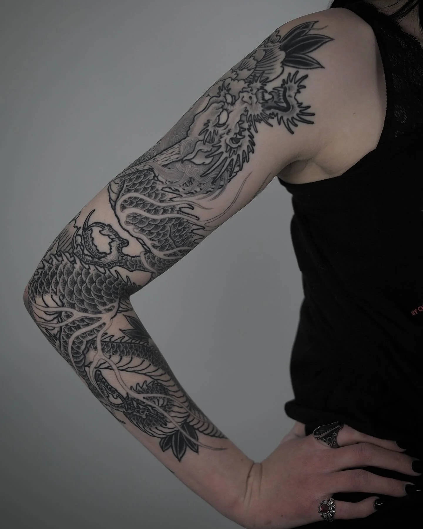 A person's arm with a black and gray tattoo of a Chinese dragon wrapping around the arm.