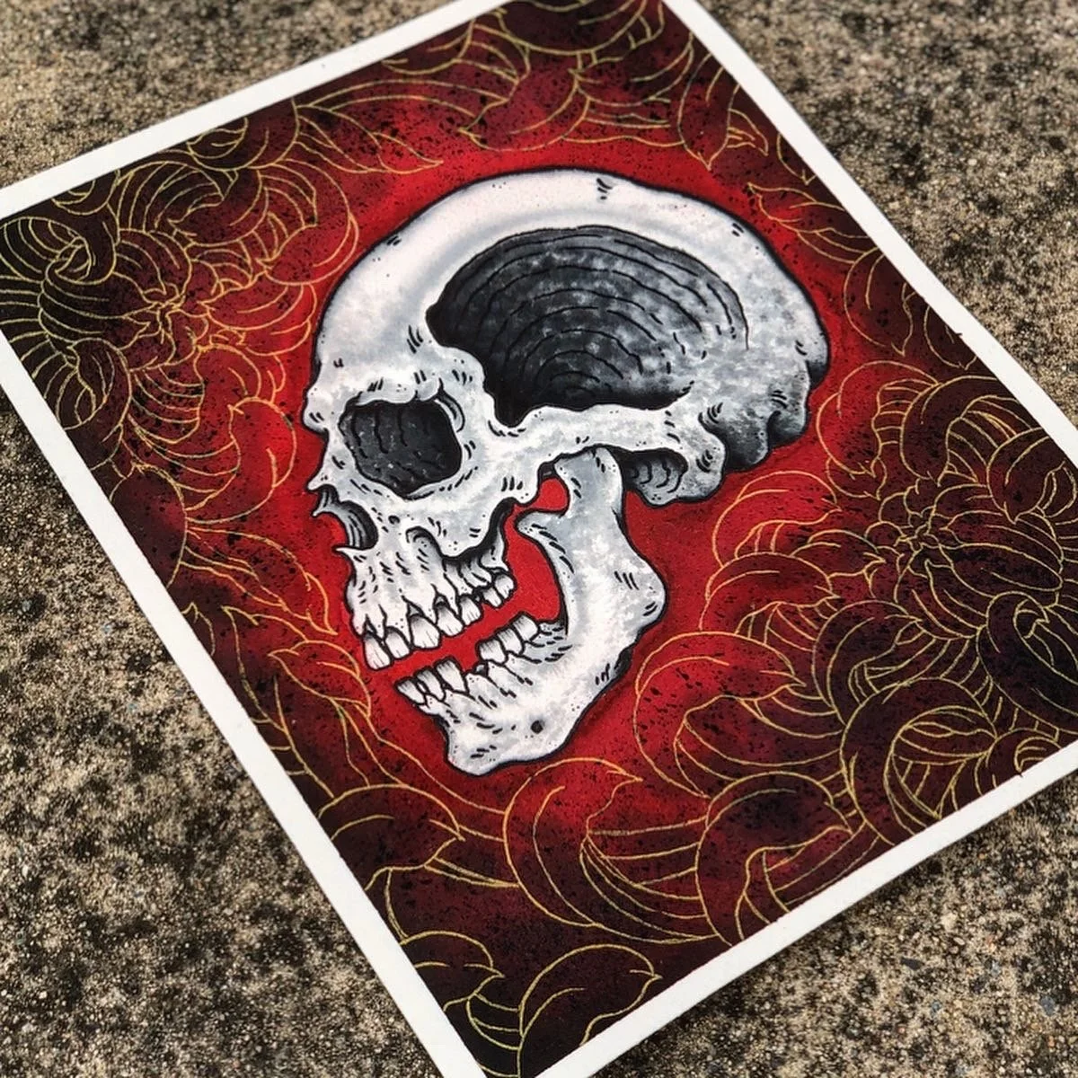 Artistic illustration of a human skull with dark shading, set against a red and black background with gold floral linework.