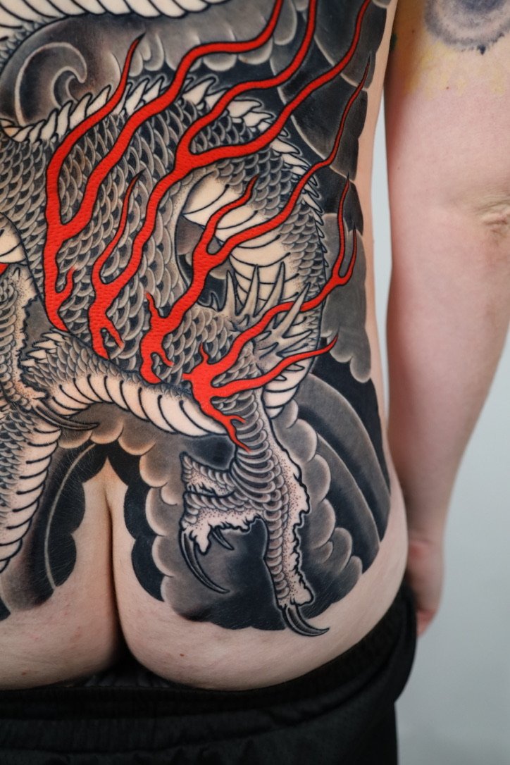 Tattoo of a dragon with black and gray shading and red accents on a person's side and back.