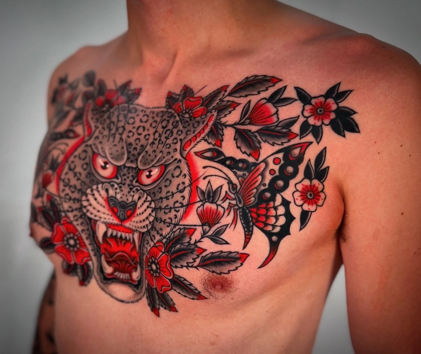 Tattoo of a leaping jaguar surrounded by flowers, leaves, and a butterfly on a man's chest.