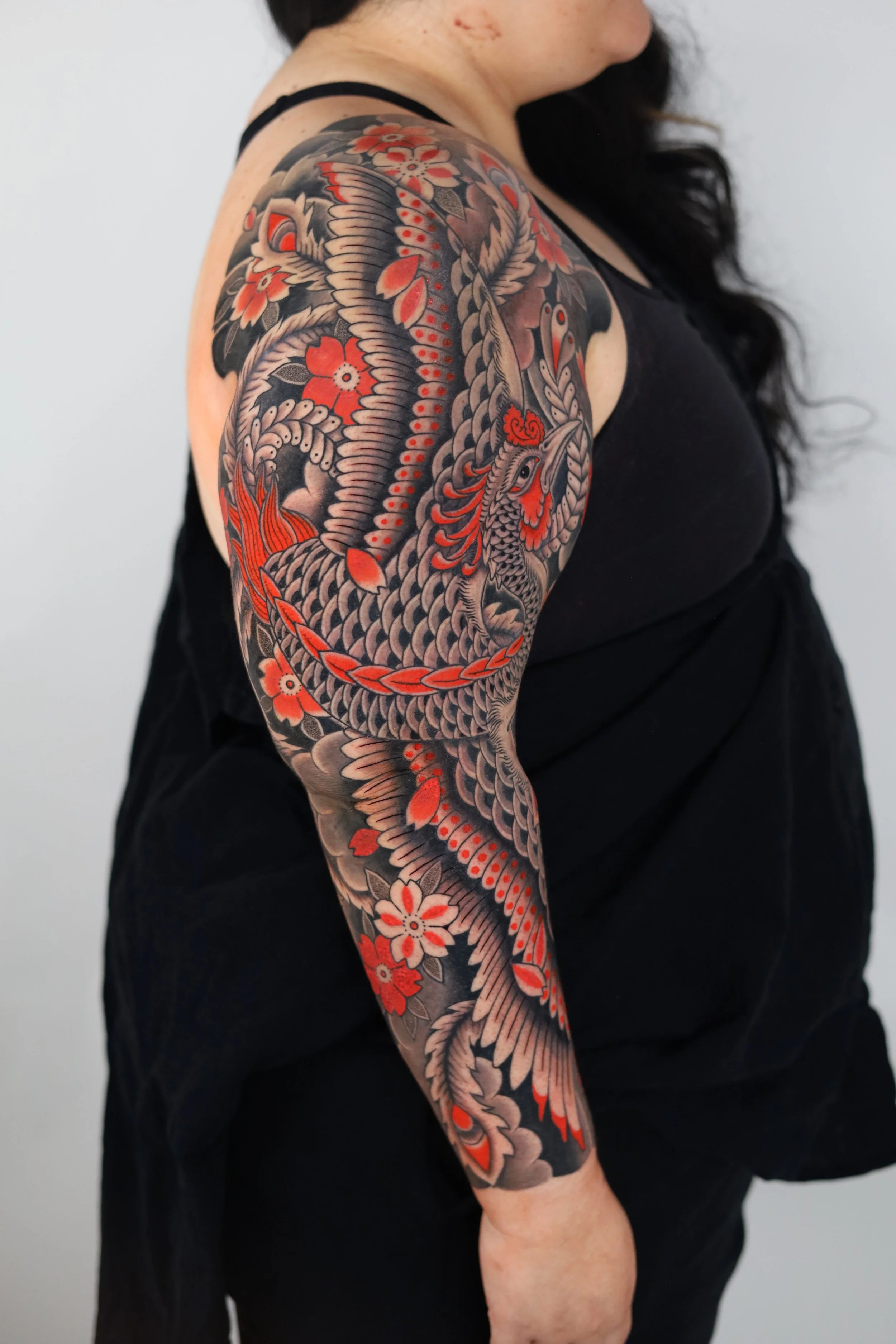 A person with a full sleeve tattoo featuring a traditional Japanese style dragon intertwined with cherry blossoms, colored primarily in black, gray, and red.