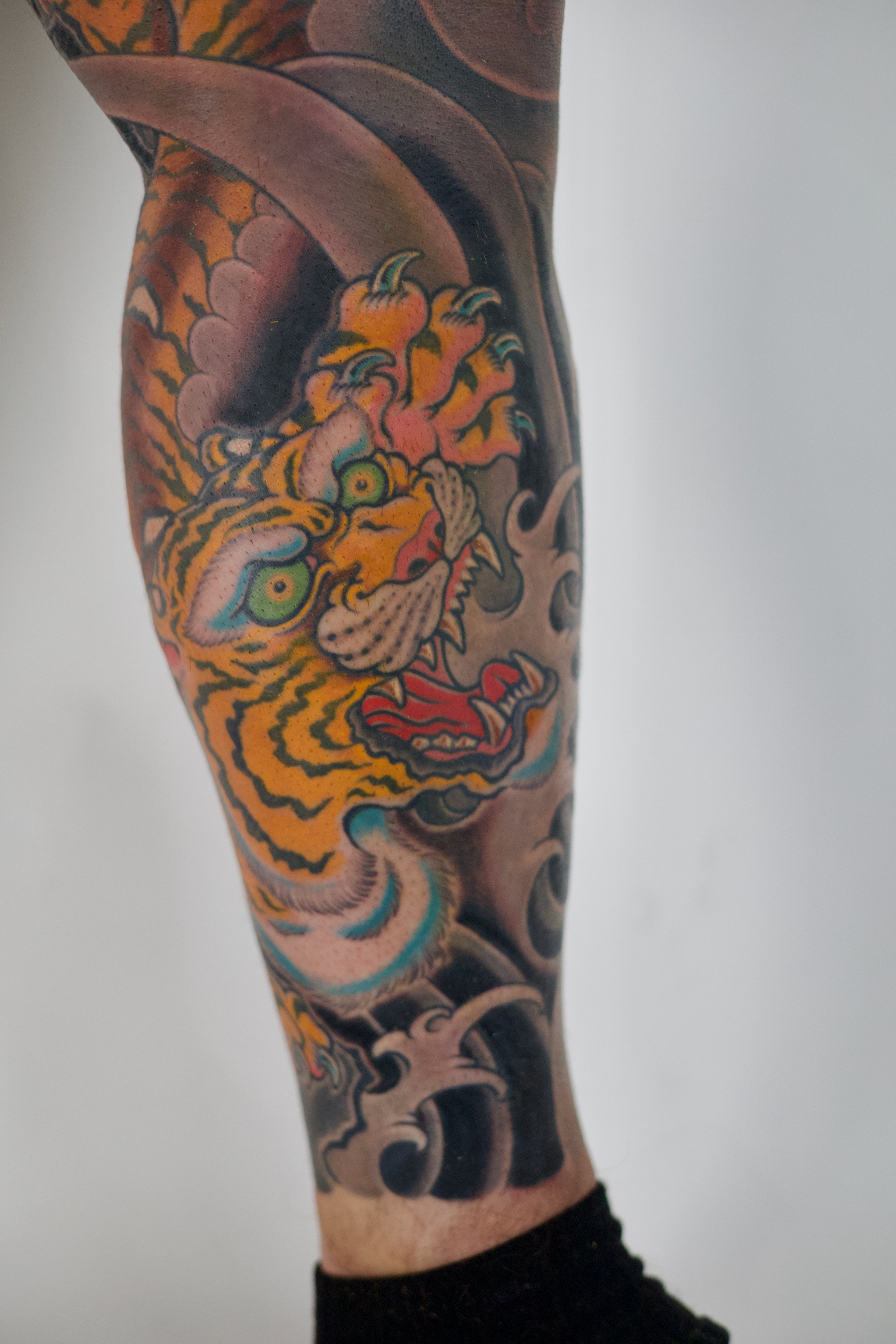 Tattoo of a fierce tiger's head with detailed fur, sharp teeth, and vibrant colors on a person's arm.