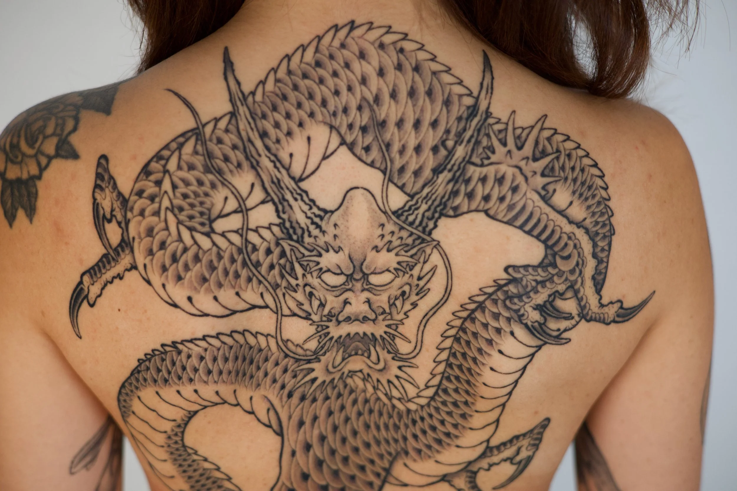 Black and gray tattoo of a fierce dragon on a person's chest and shoulder with detailed scales and sharp claws.