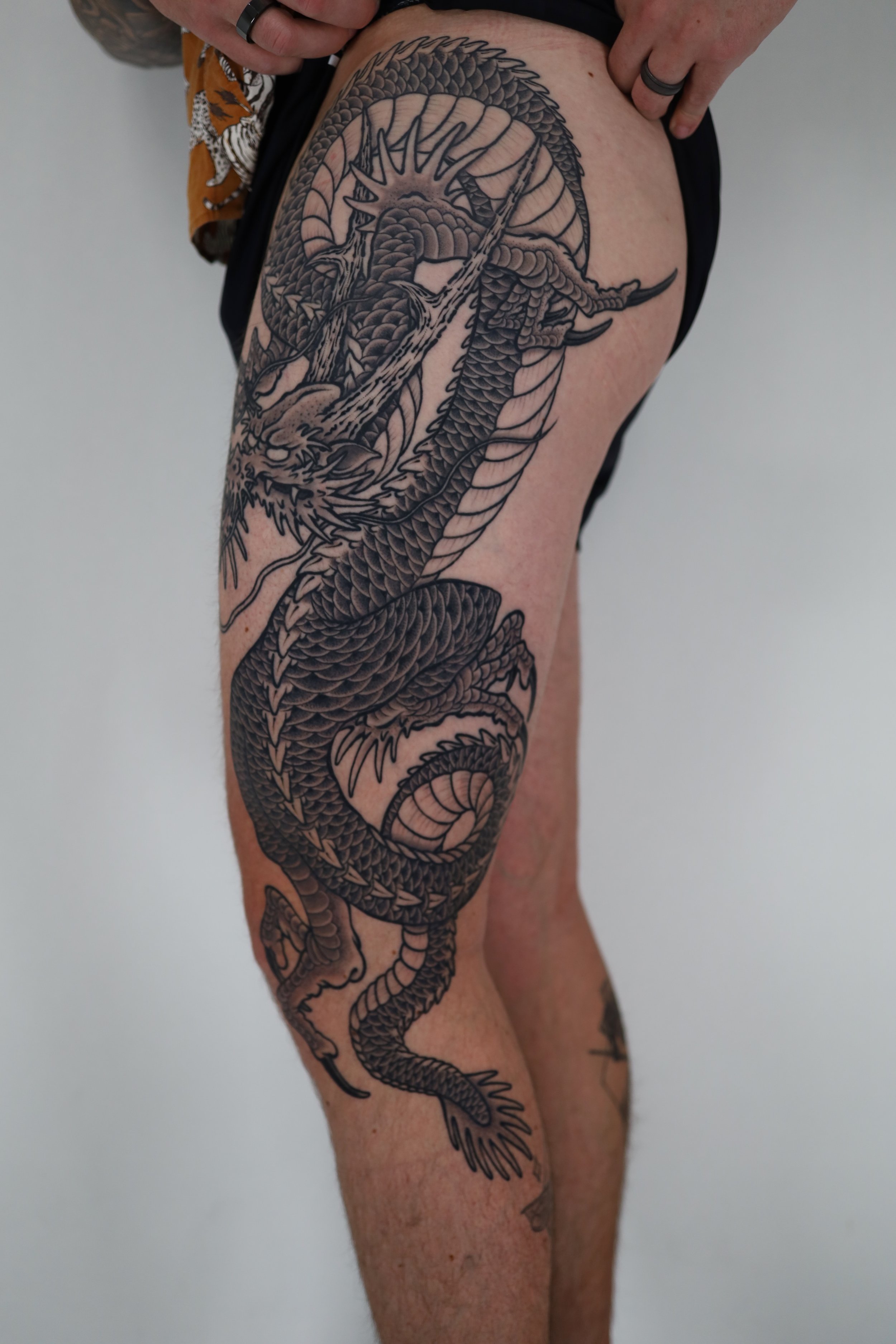 A person's leg with a large black and gray tattoo of a dragon wrapped around the thigh and leg.