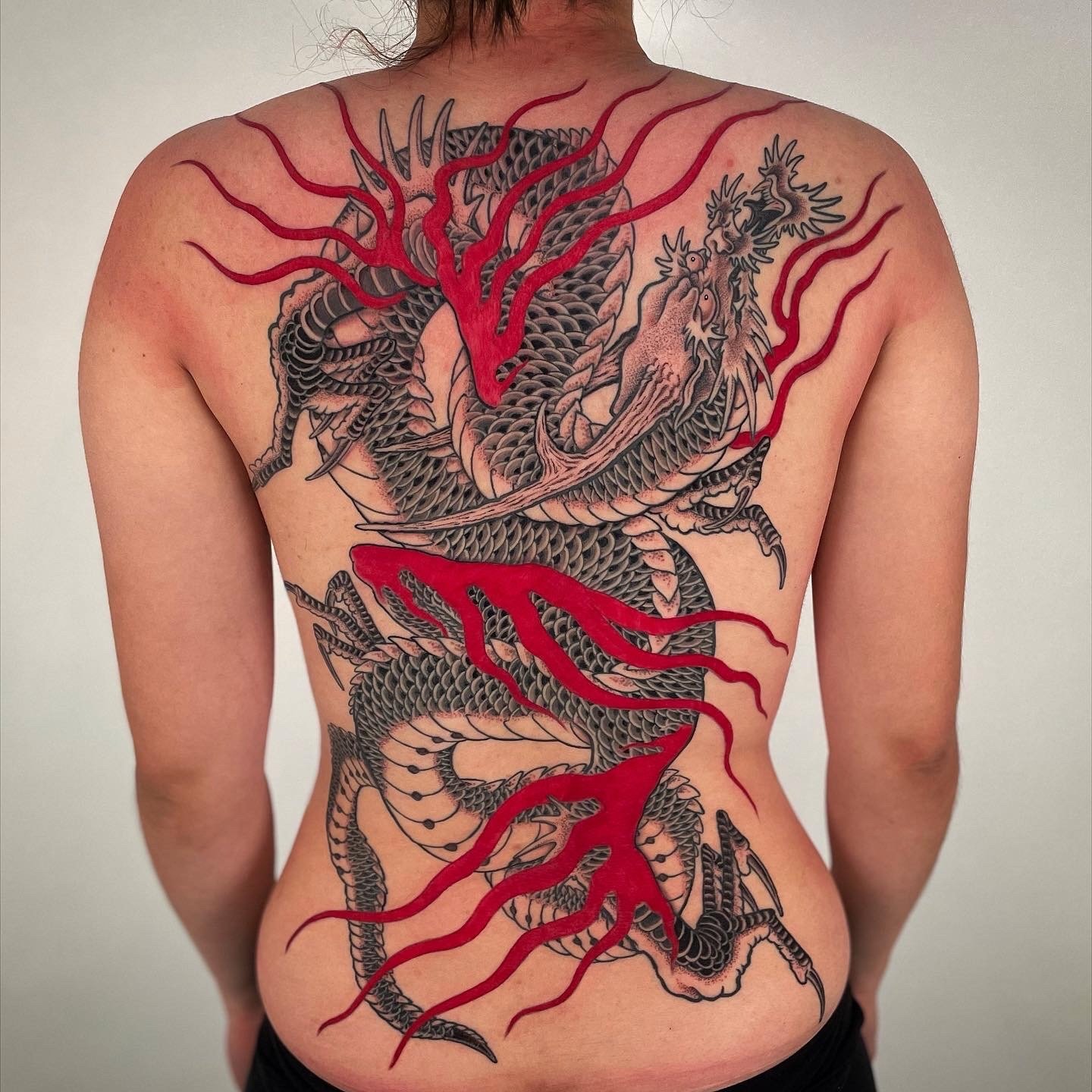 A person with a large, intricate black and red dragon tattoo covering most of their back.
