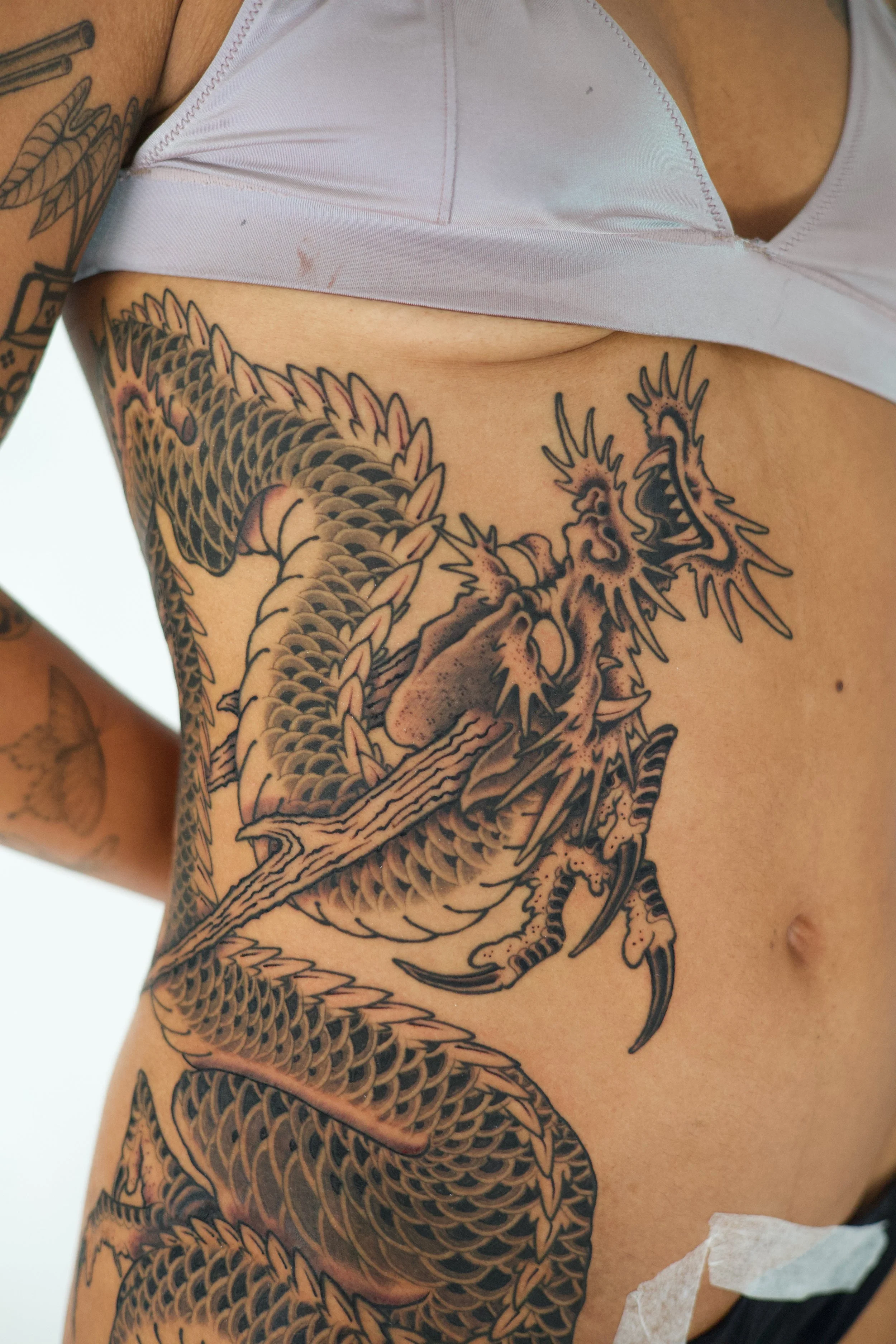 Close-up of a person's side torso with a detailed black ink dragon tattoo.