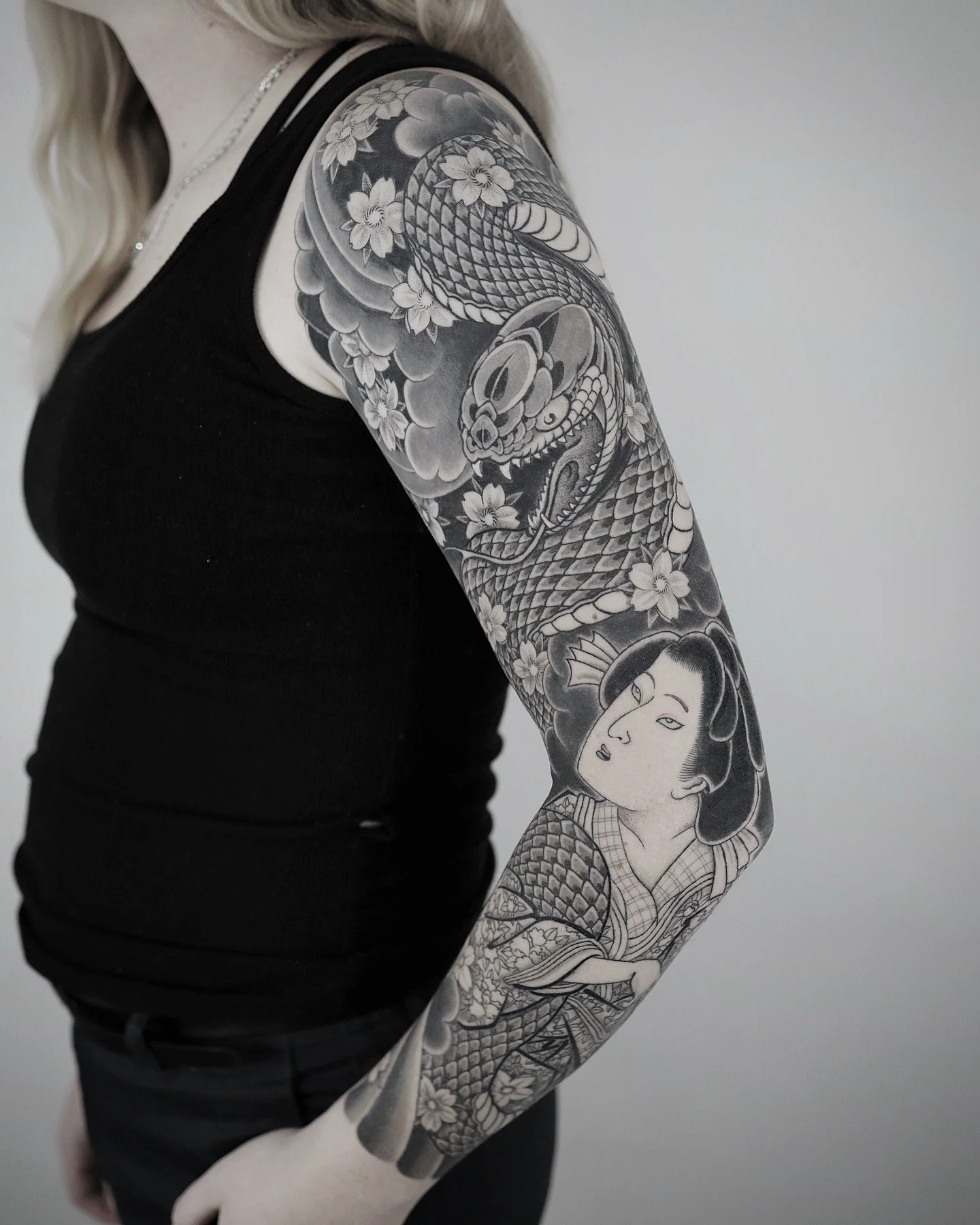 Black and gray tattoo sleeve featuring a snake, a skull, clouds, and a woman in traditional Japanese style.