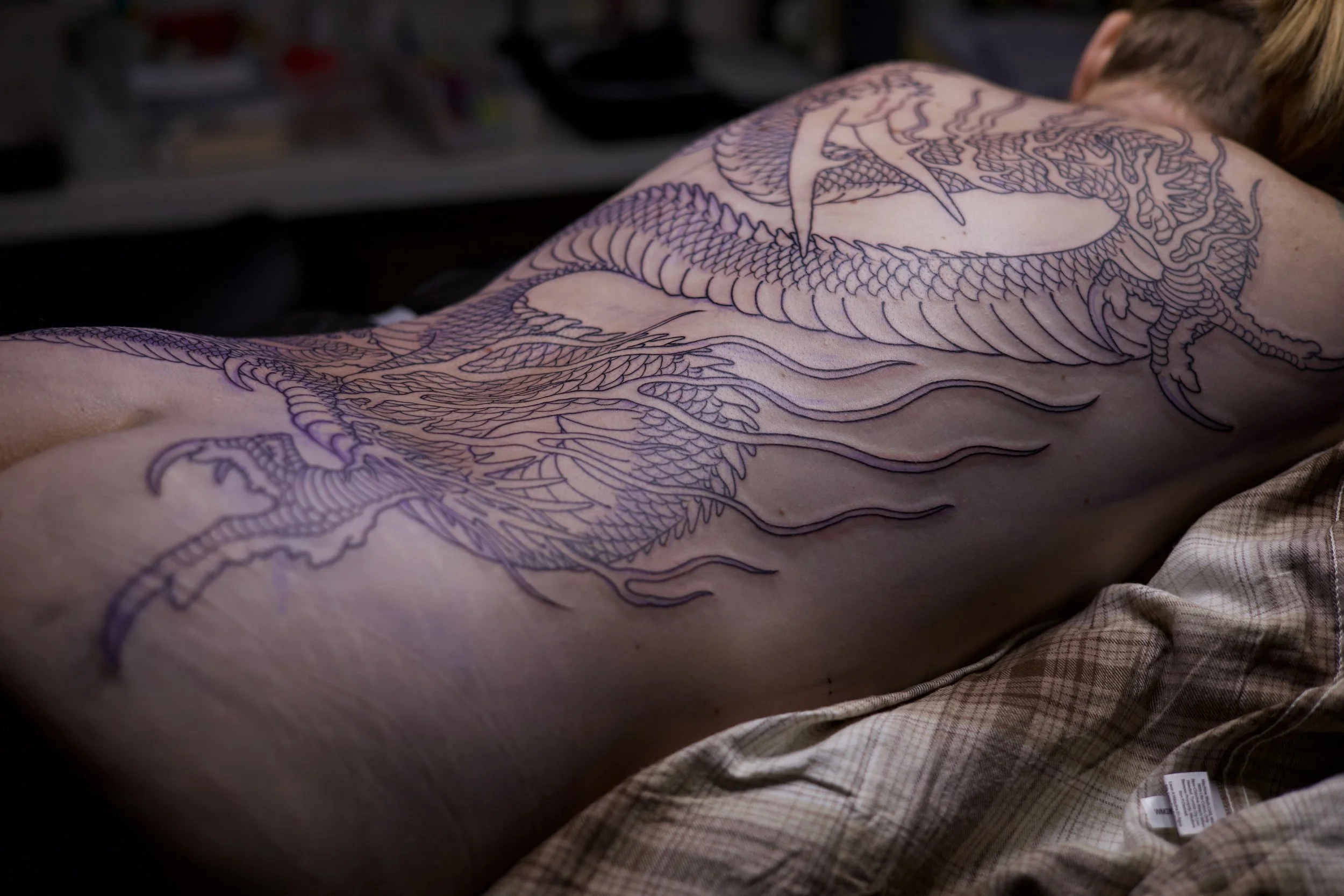 A person's back with an outline of a dragon tattoo preparing to be inked.