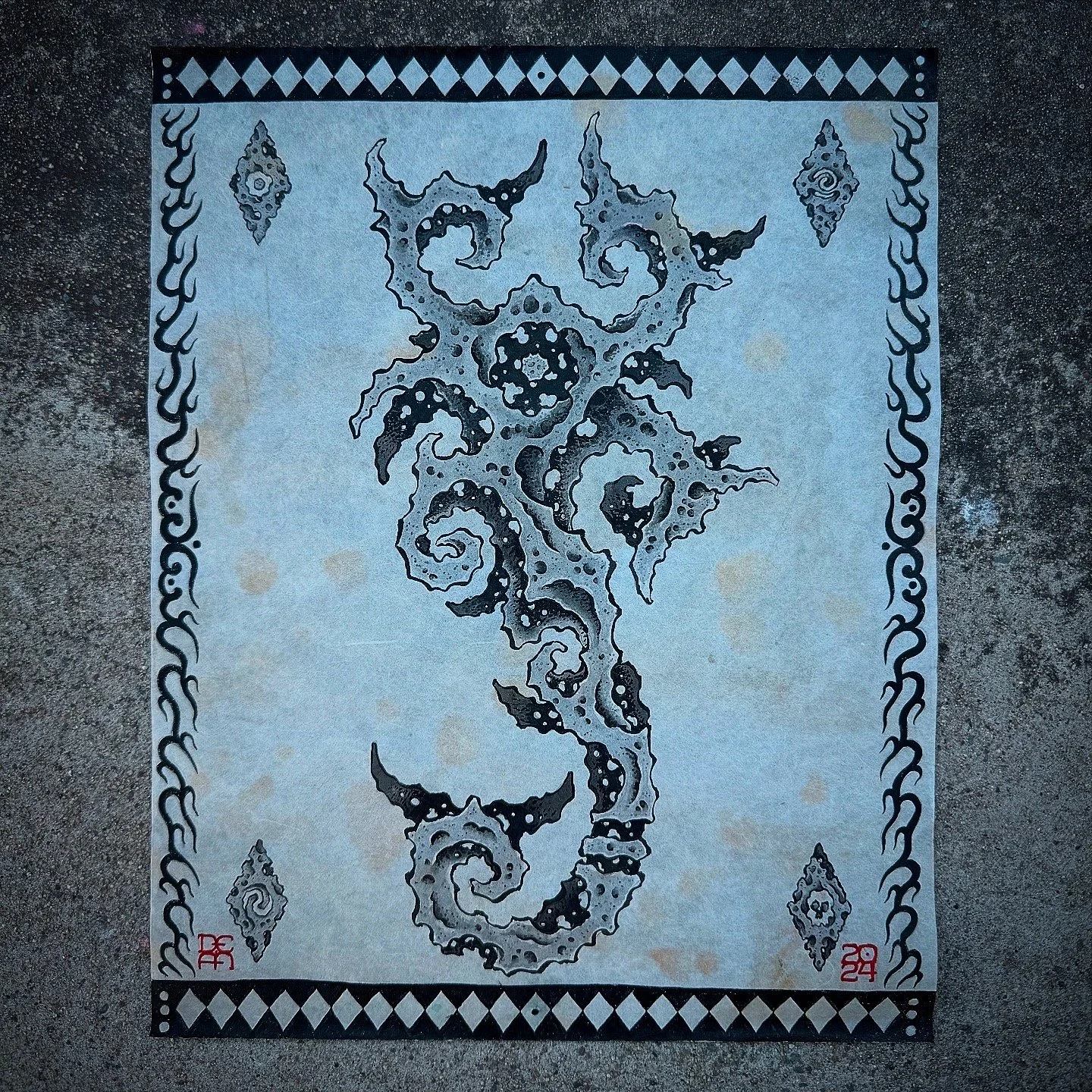 A decorative rug with black and white swirling patterns and diamond shapes along the border, placed on a concrete surface.