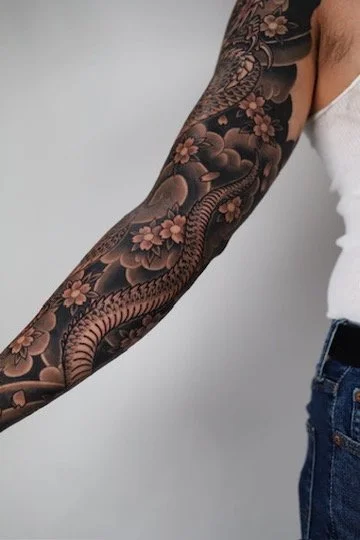 Arm tattoo featuring a snake and cherry blossoms.