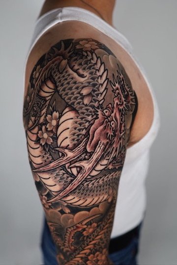 Tattoo of a dragon with flowers and clouds on a person's upper arm.