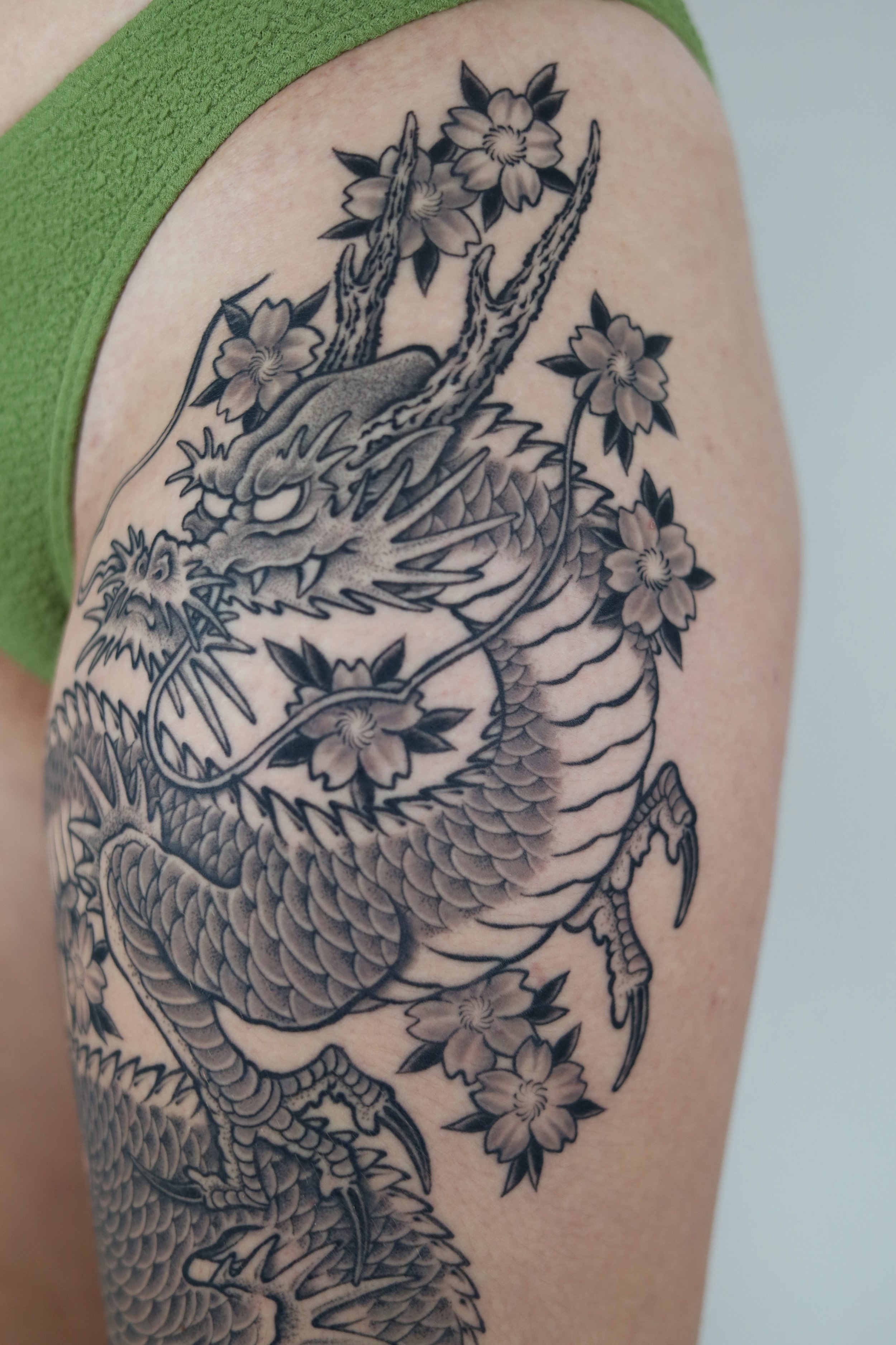 Tattoo of a traditional Japanese dragon intertwined among cherry blossoms on a person's upper arm.