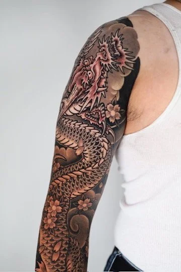 Close-up of a person's arm with a detailed dragon tattoo surrounded by cherry blossoms.